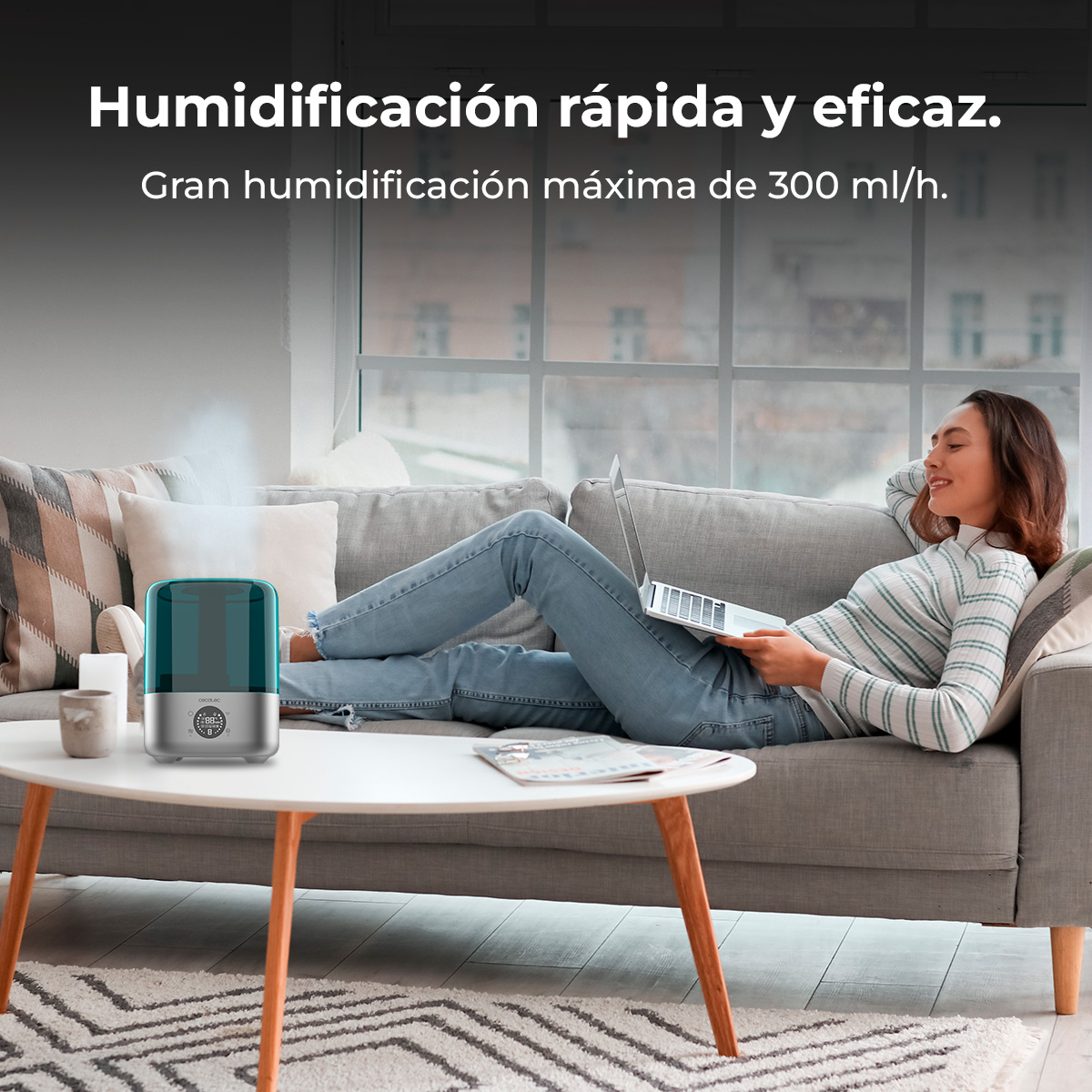 Una mujer se relaja en un sofá con un portátil, mientras un humidificador en la mesa emite vapor.