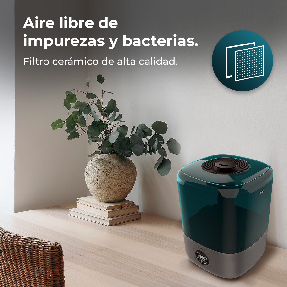 Un humidificador verde azulado sobre una mesa de madera junto a un jarrón con plantas sobre libros.