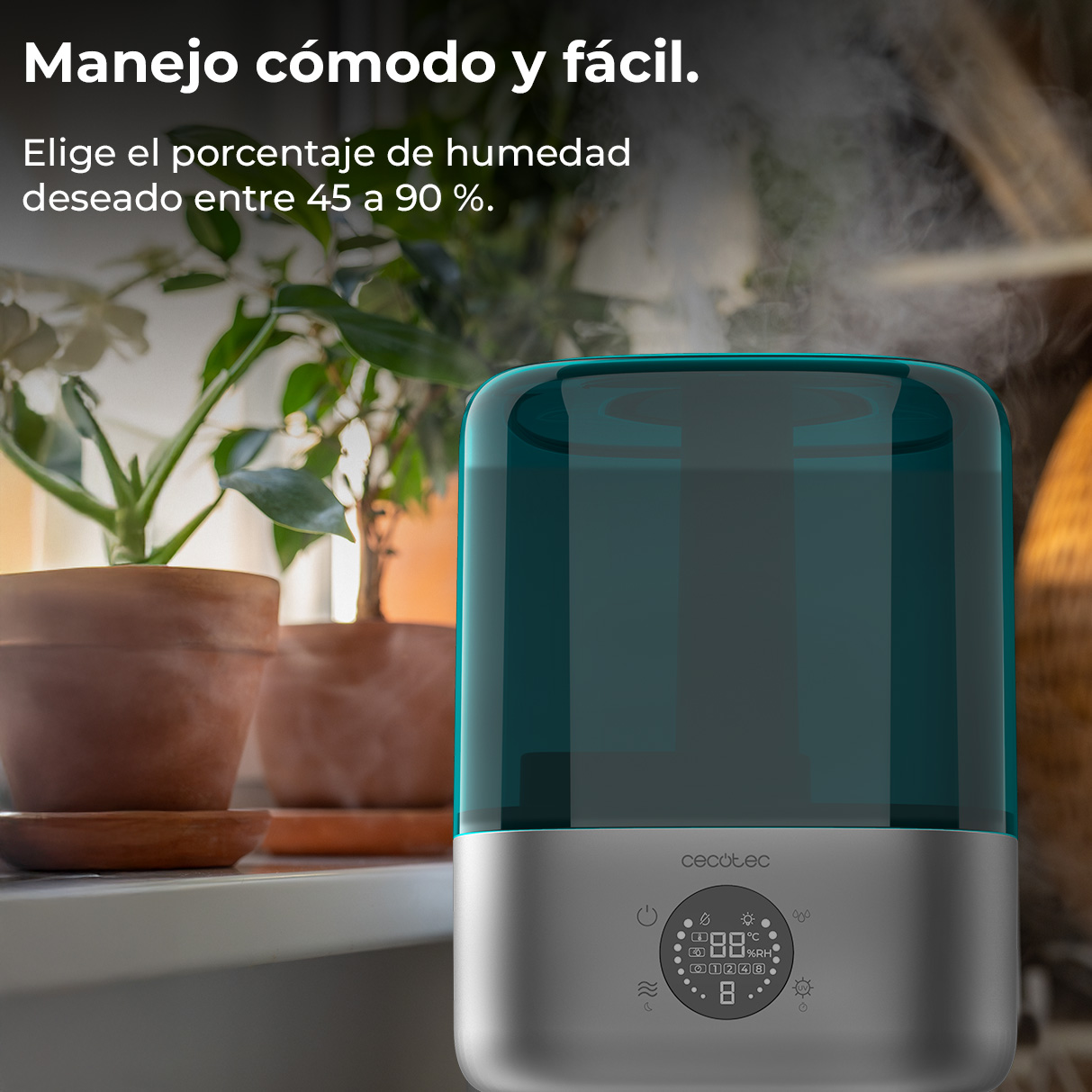 Un humidificador verde azulado y plateado emite vapor junto a plantas en maceta en el alféizar.