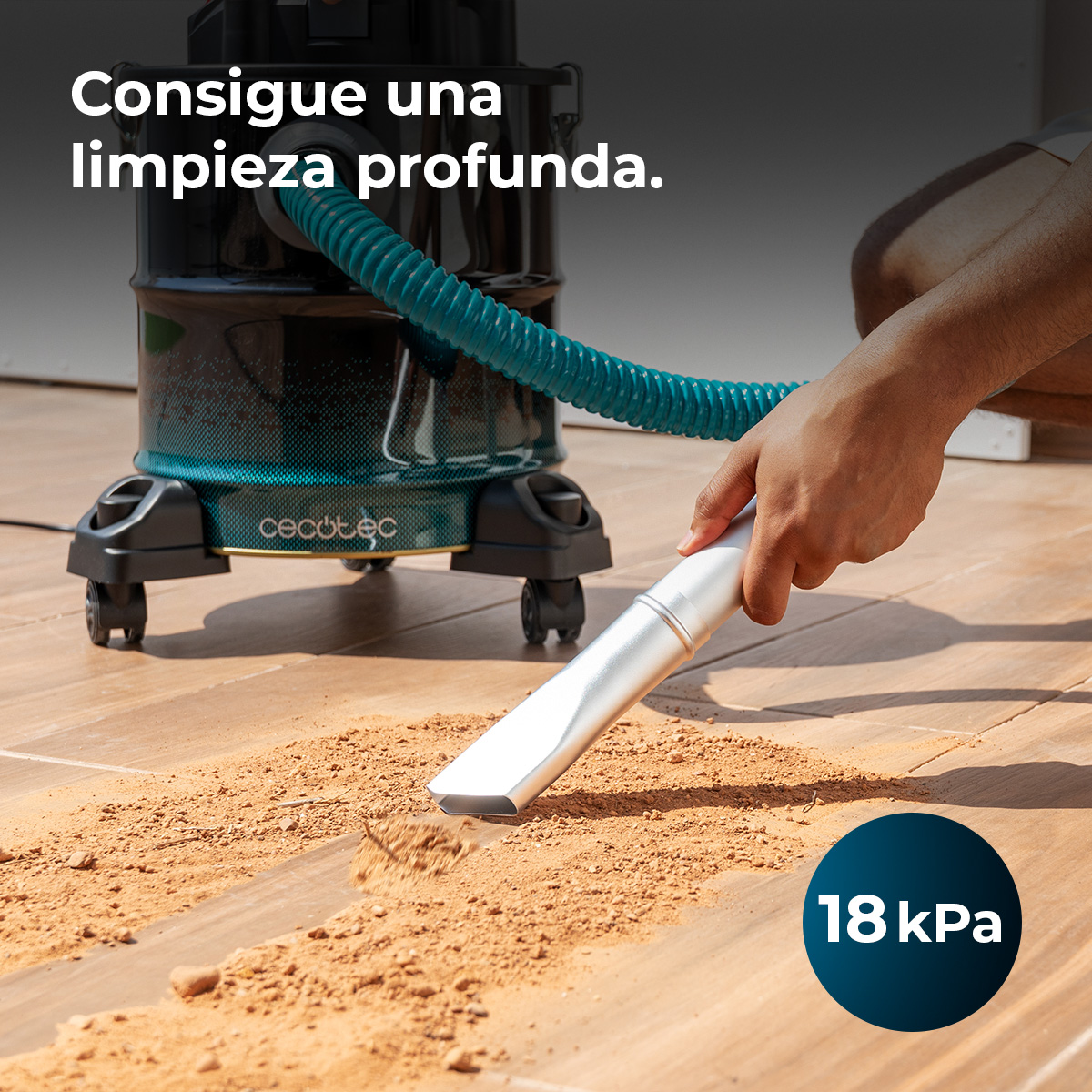 Una persona aspira suciedad de un suelo de madera con un aspirador negro y manguera azul.