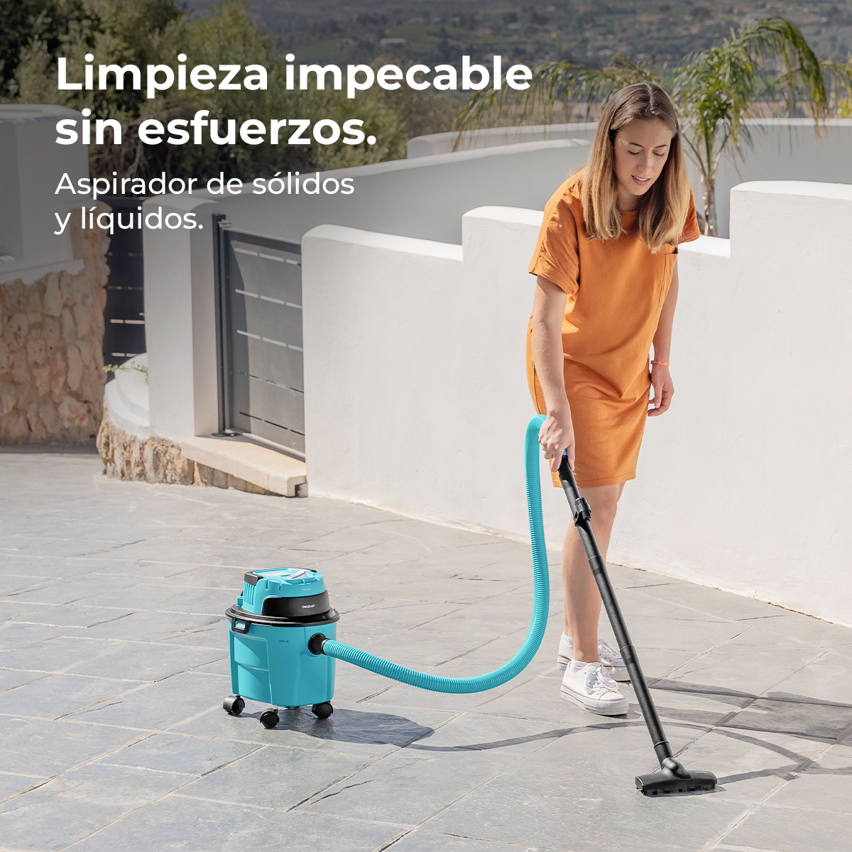 Mujer con vestido naranja limpia la terraza con un aspirador azul.