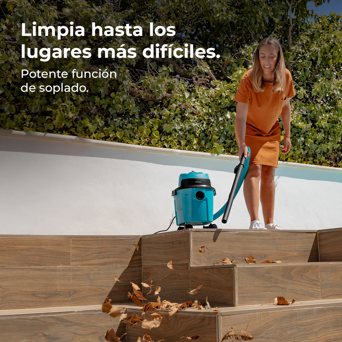 Una mujer de naranja usa una aspiradora azul para limpiar hojas en escaleras de madera.