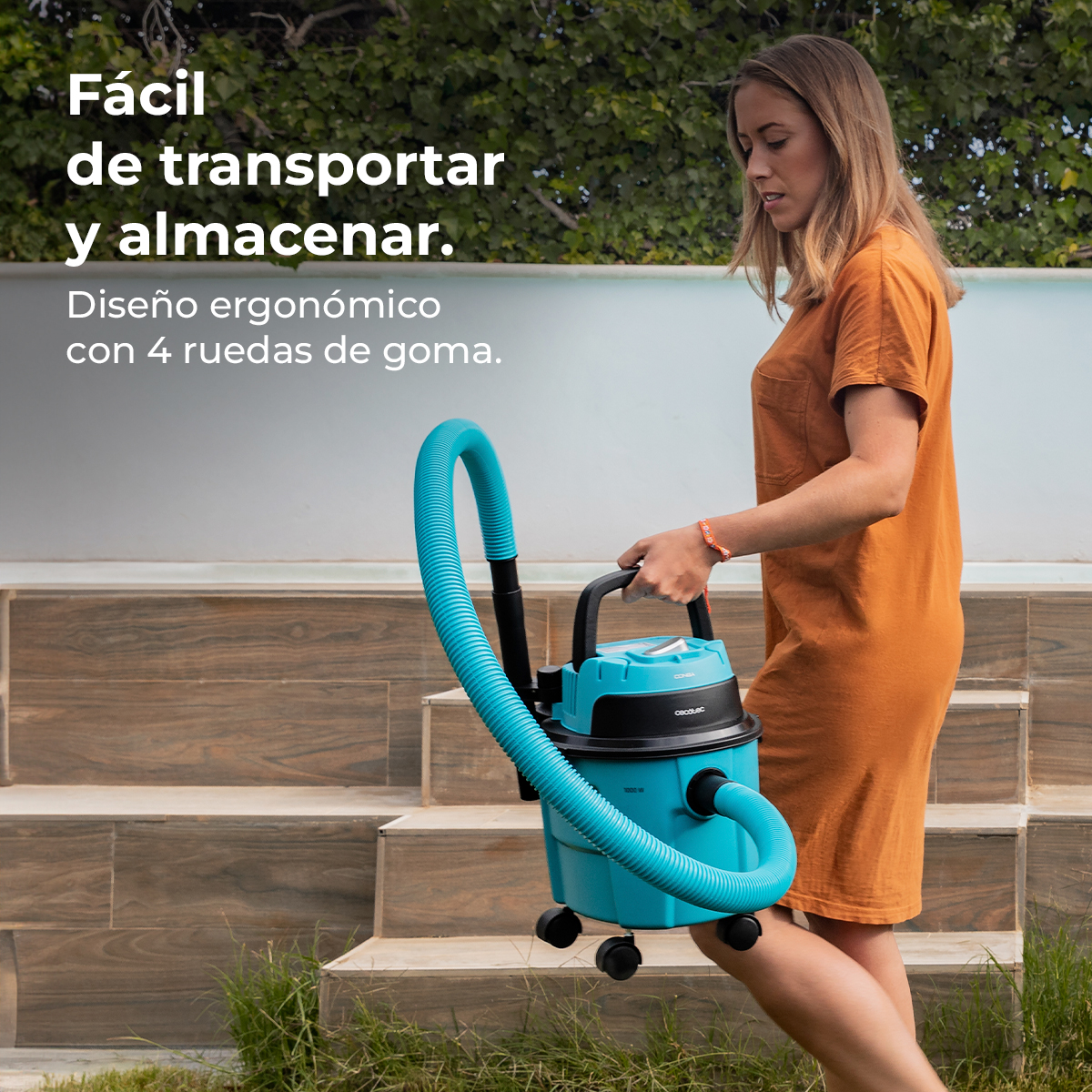 Una mujer con vestido naranja lleva una aspiradora azul de suelo cerca de unas escaleras.