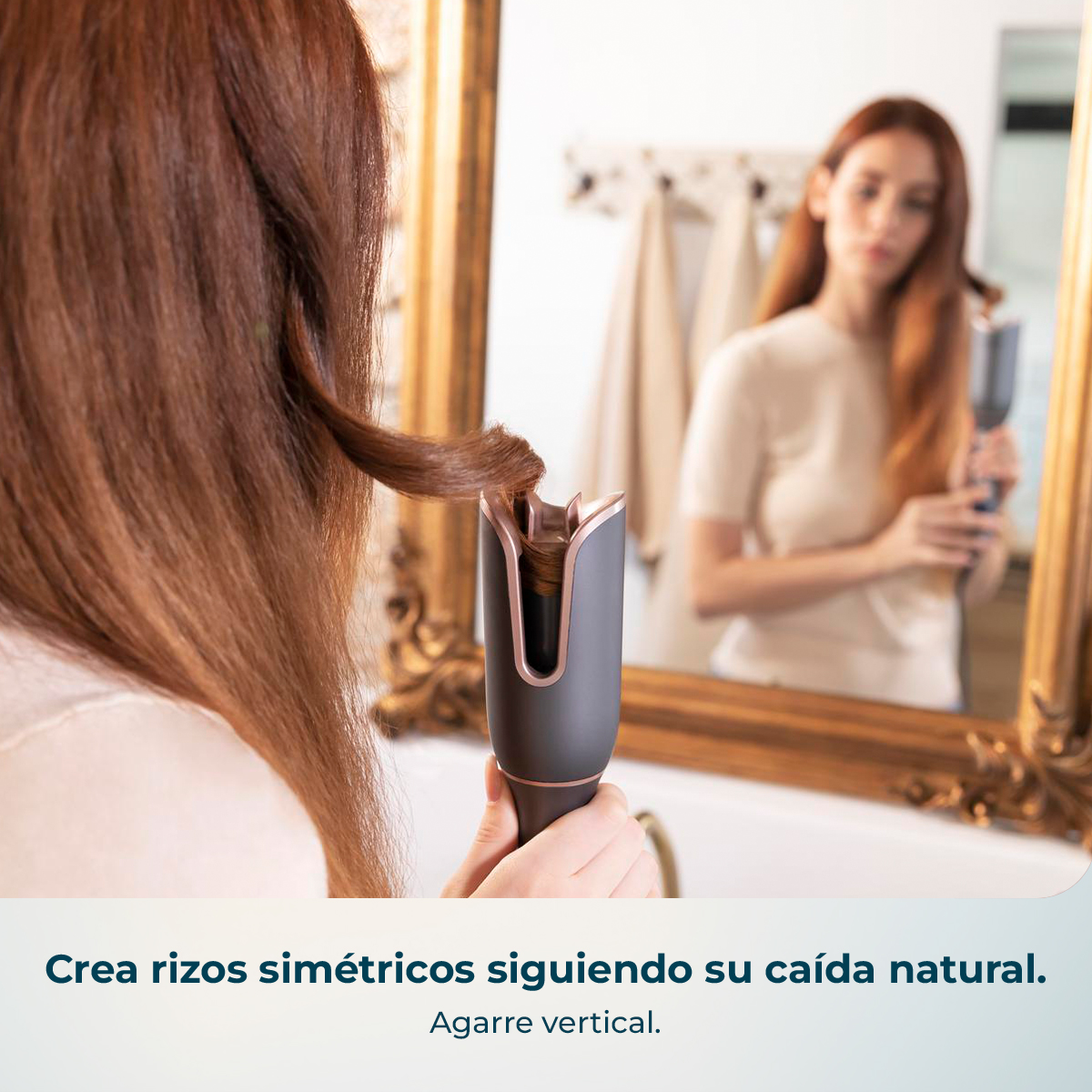 Una mujer peina su cabello castaño con un rizador automático frente a un espejo.