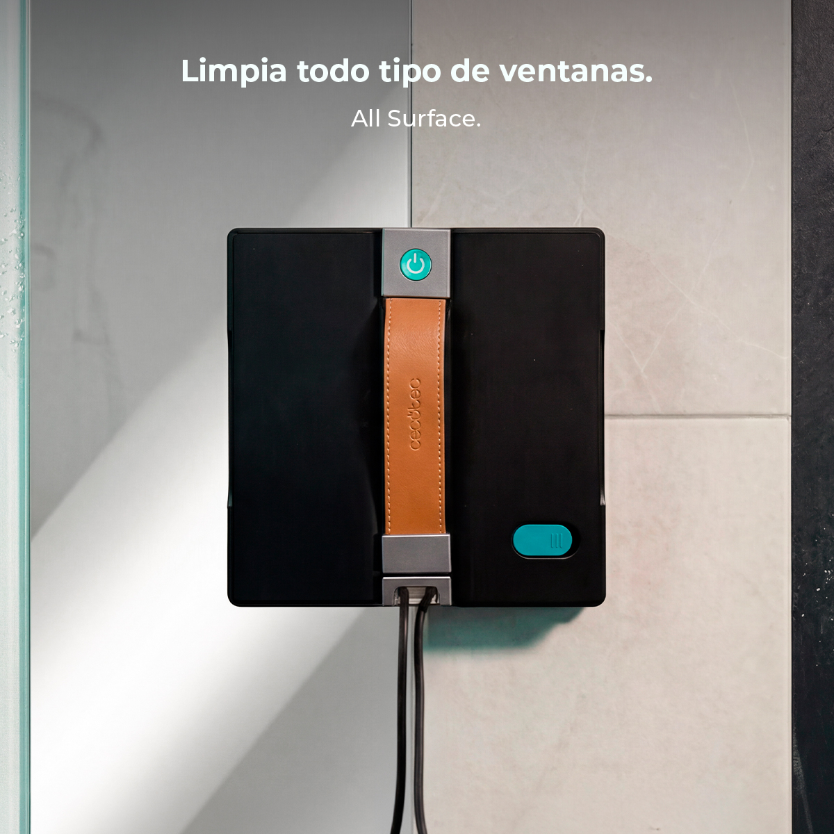 Un robot limpiador de ventanas negro con asa de cuero marrón adherido a una pared de azulejos.