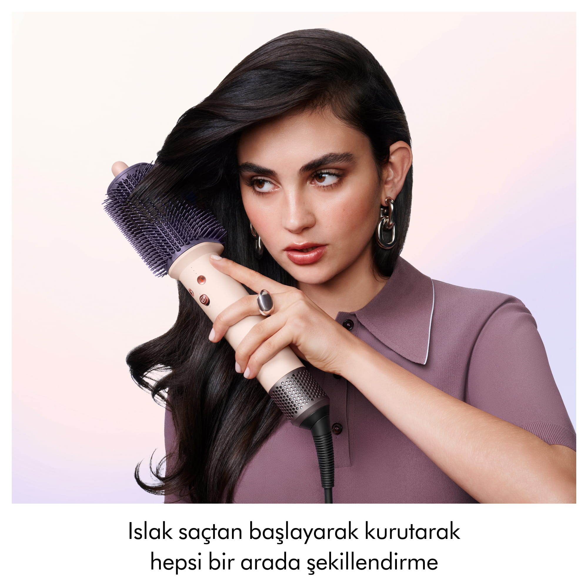 Bir kadın açık arka plan önünde mor saç şekillendiriciyle uzun koyu saçlarını şekillendiriyor.
