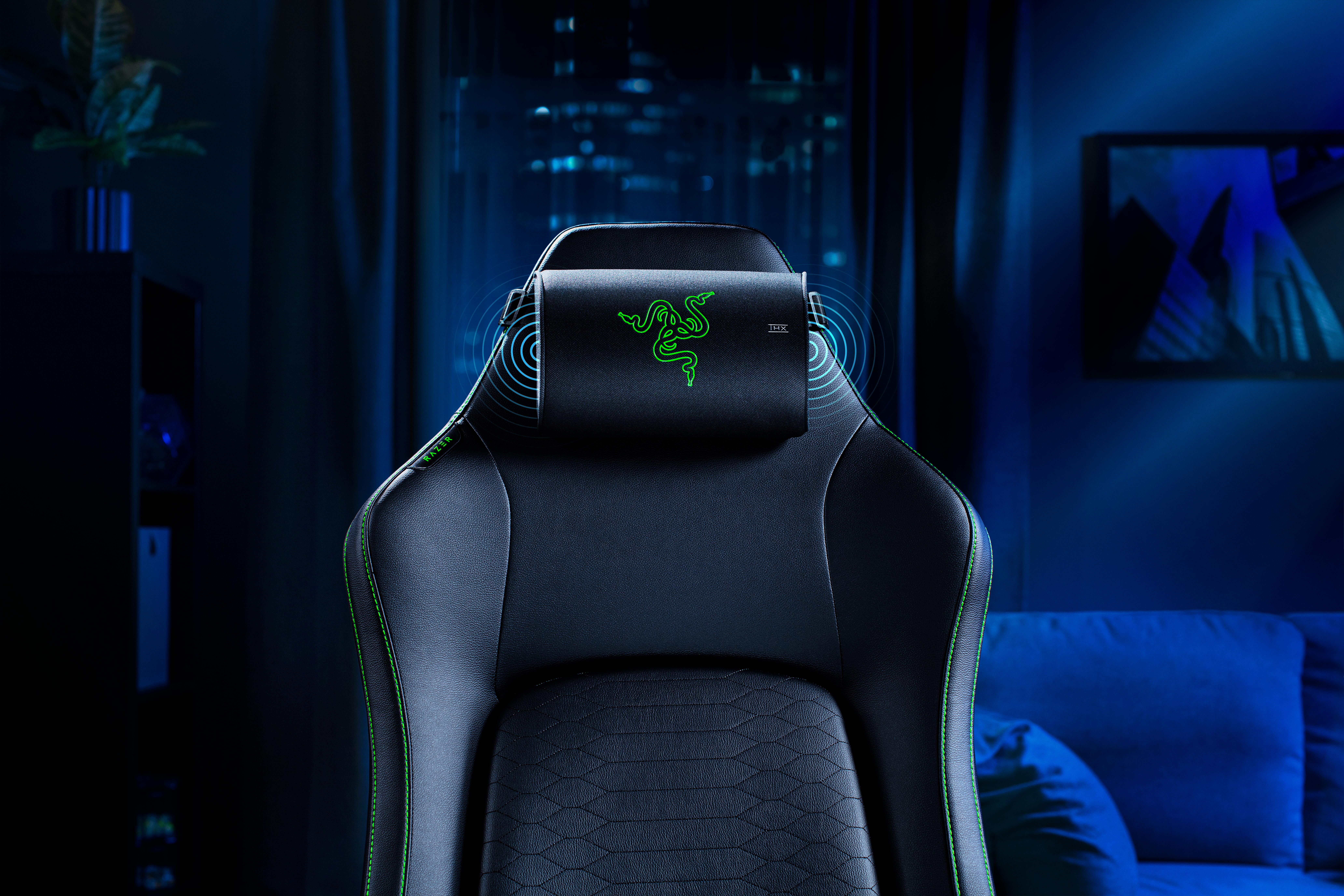 Ein schwarzer Gaming-Stuhl mit grünen Nähten und Razer-Logo auf der Kopfstütze in einem blau beleuchteten Raum.