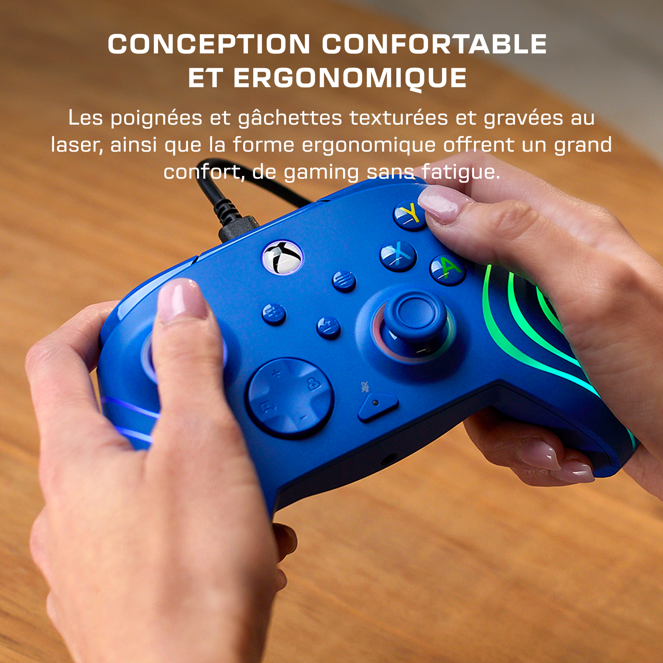 Une personne tient une manette Xbox filaire bleue sur une surface en bois.