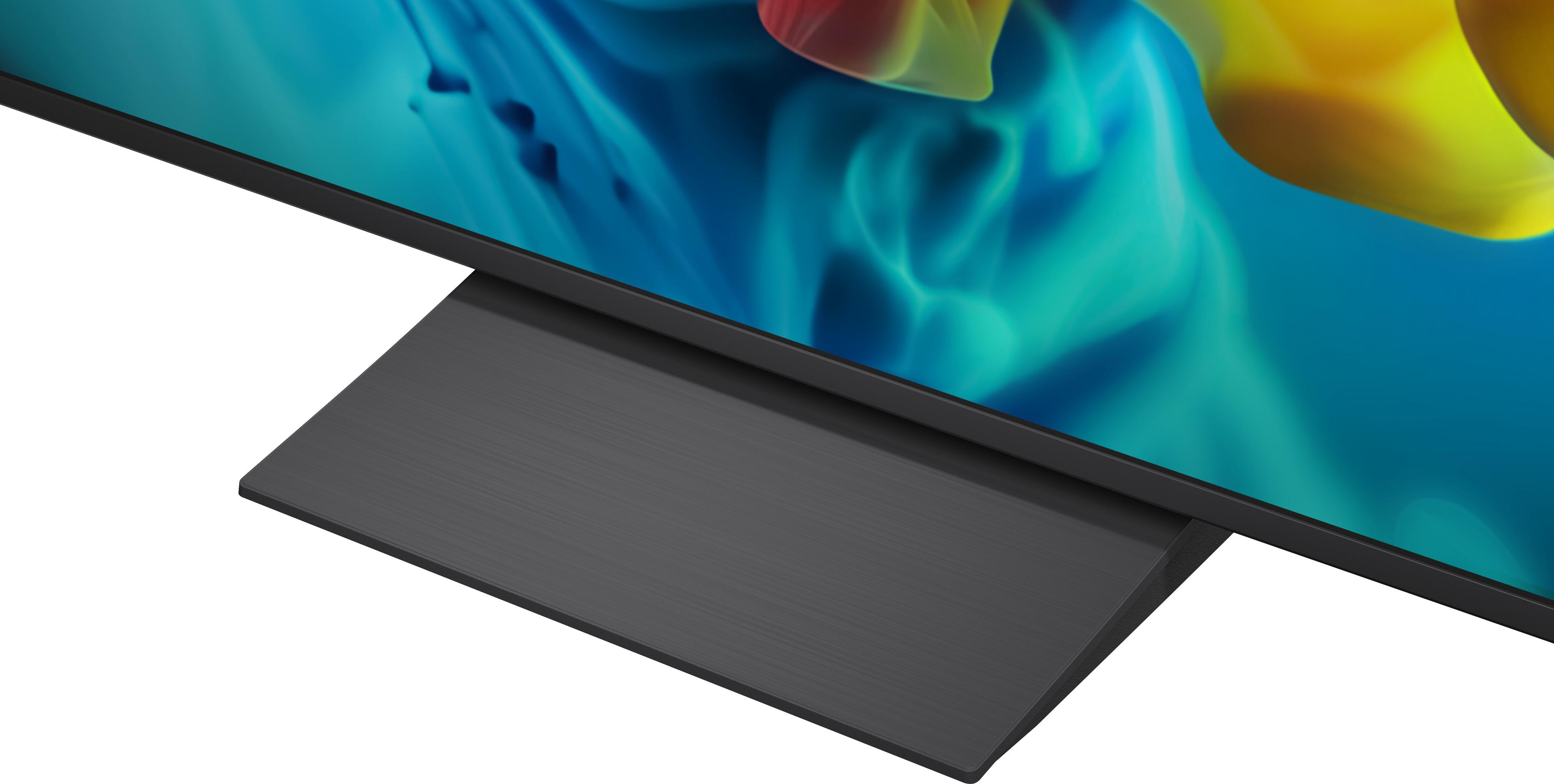 Ein Fernseher mit schwarzem Metallstandfuß und einem bunten abstrakten Bild auf dem Bildschirm.