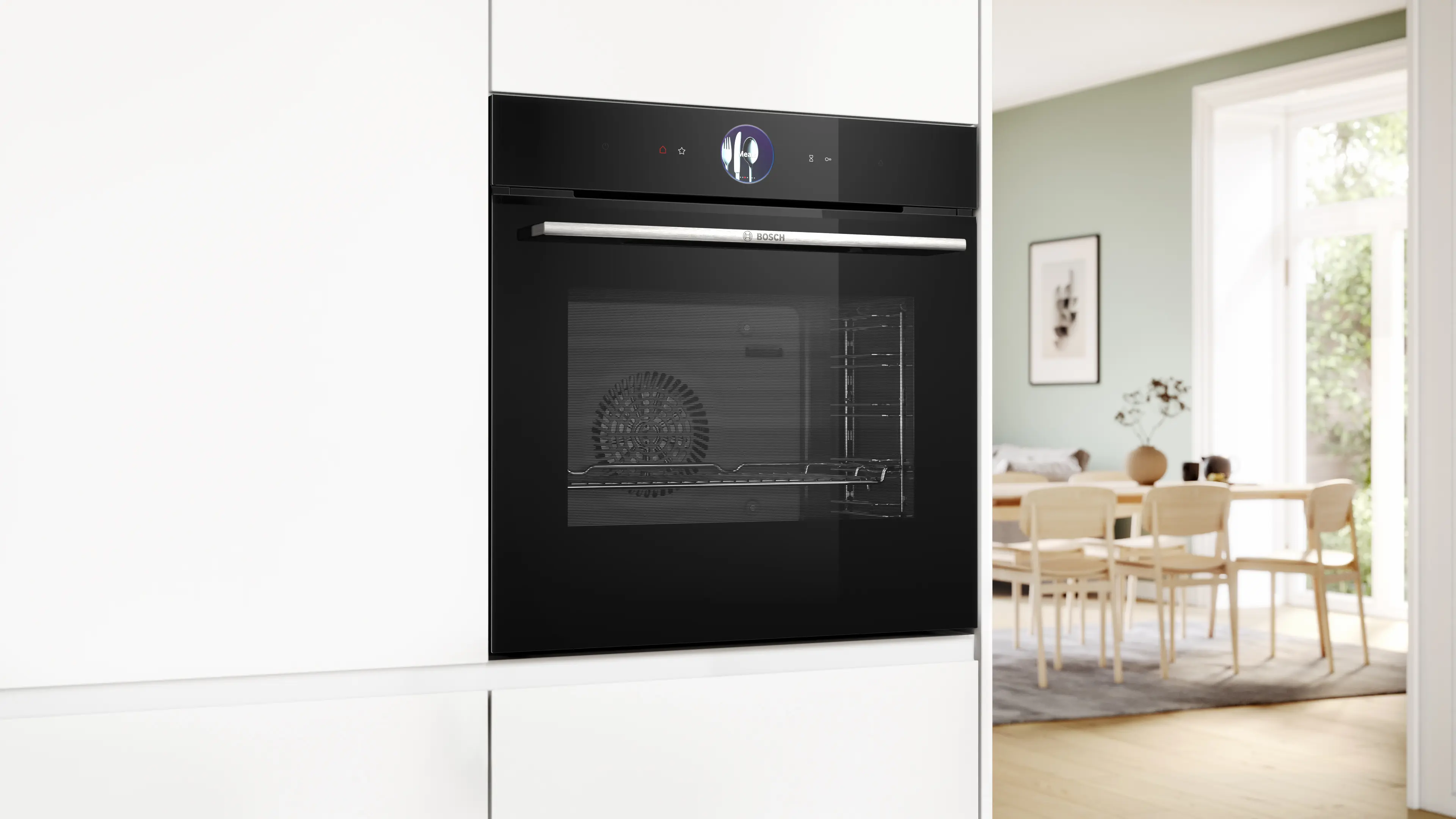 Un horno empotrable Bosch negro en una cocina blanca, con un comedor luminoso al fondo.