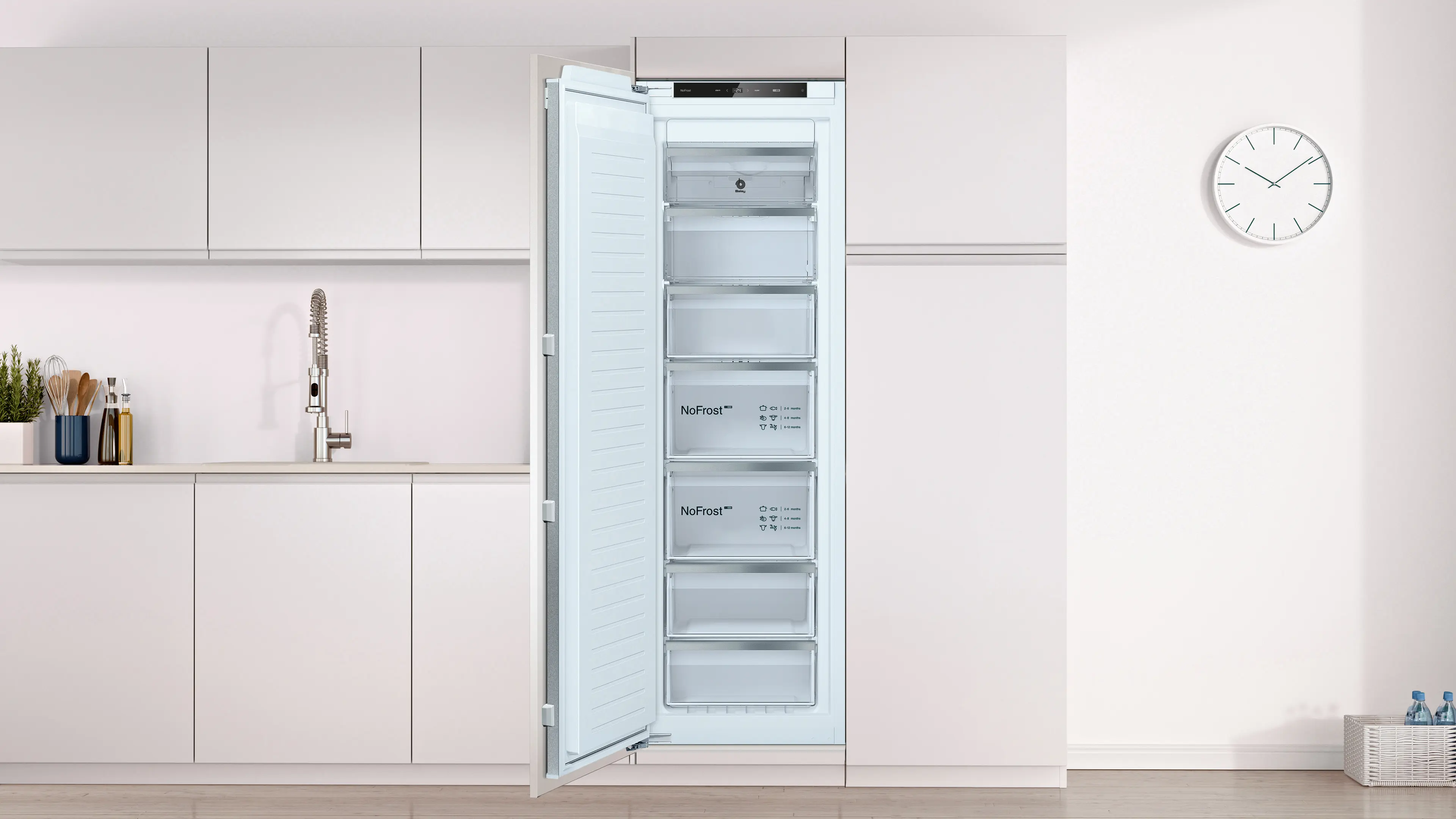 Un congelador empotrable blanco con la puerta abierta en una cocina moderna con armarios blancos y un reloj de pared.