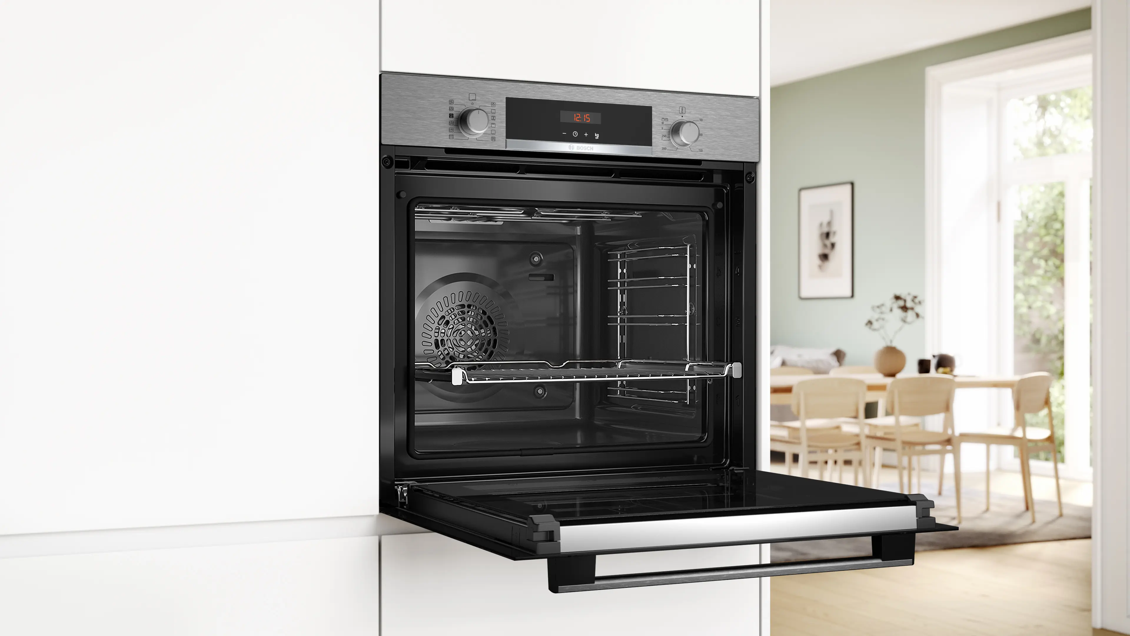 Un horno empotrable Bosch con la puerta abierta, en un mueble de cocina blanco y comedor al fondo.