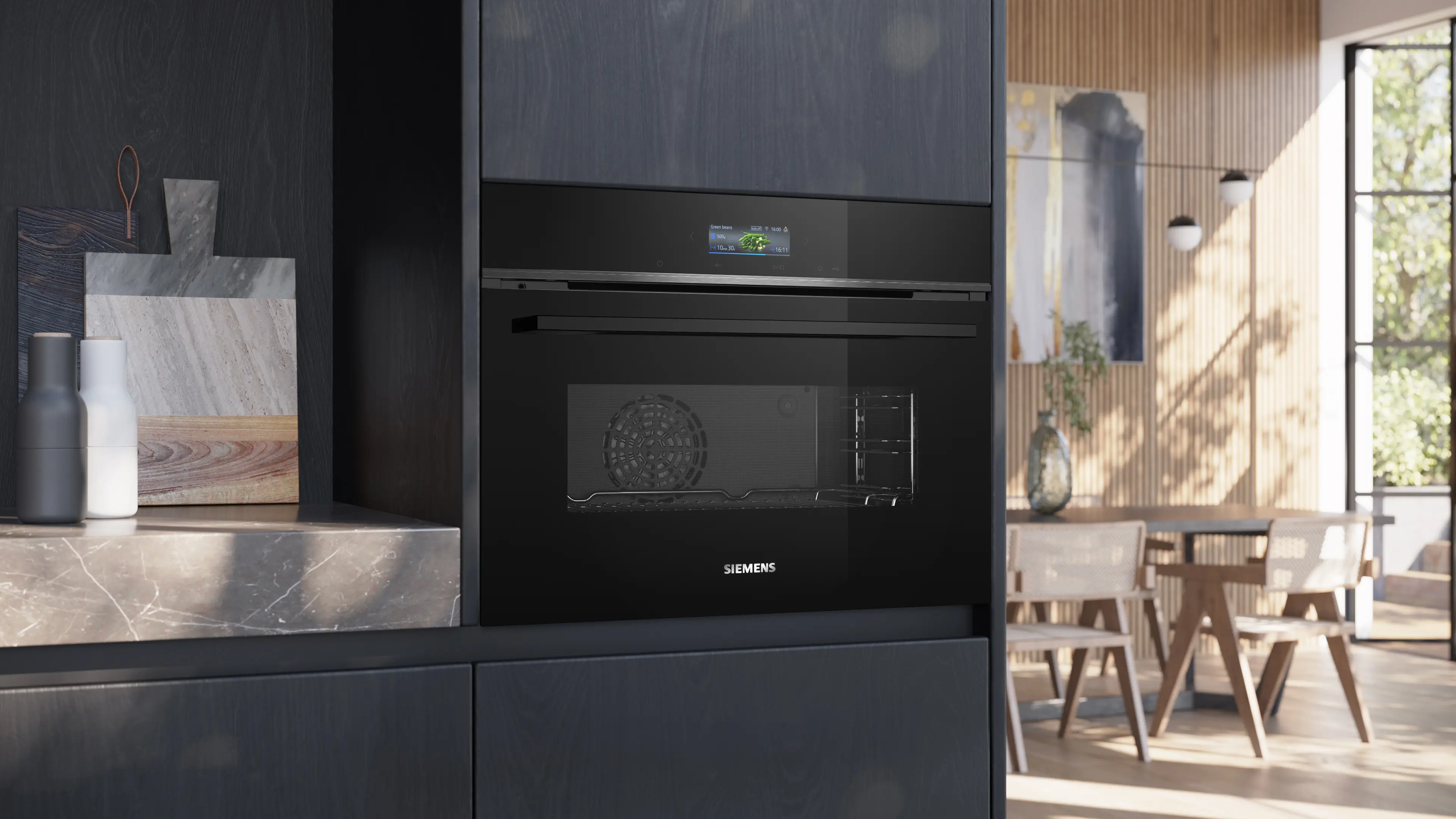 Un horno empotrable Siemens negro en una cocina moderna con comedor al fondo.