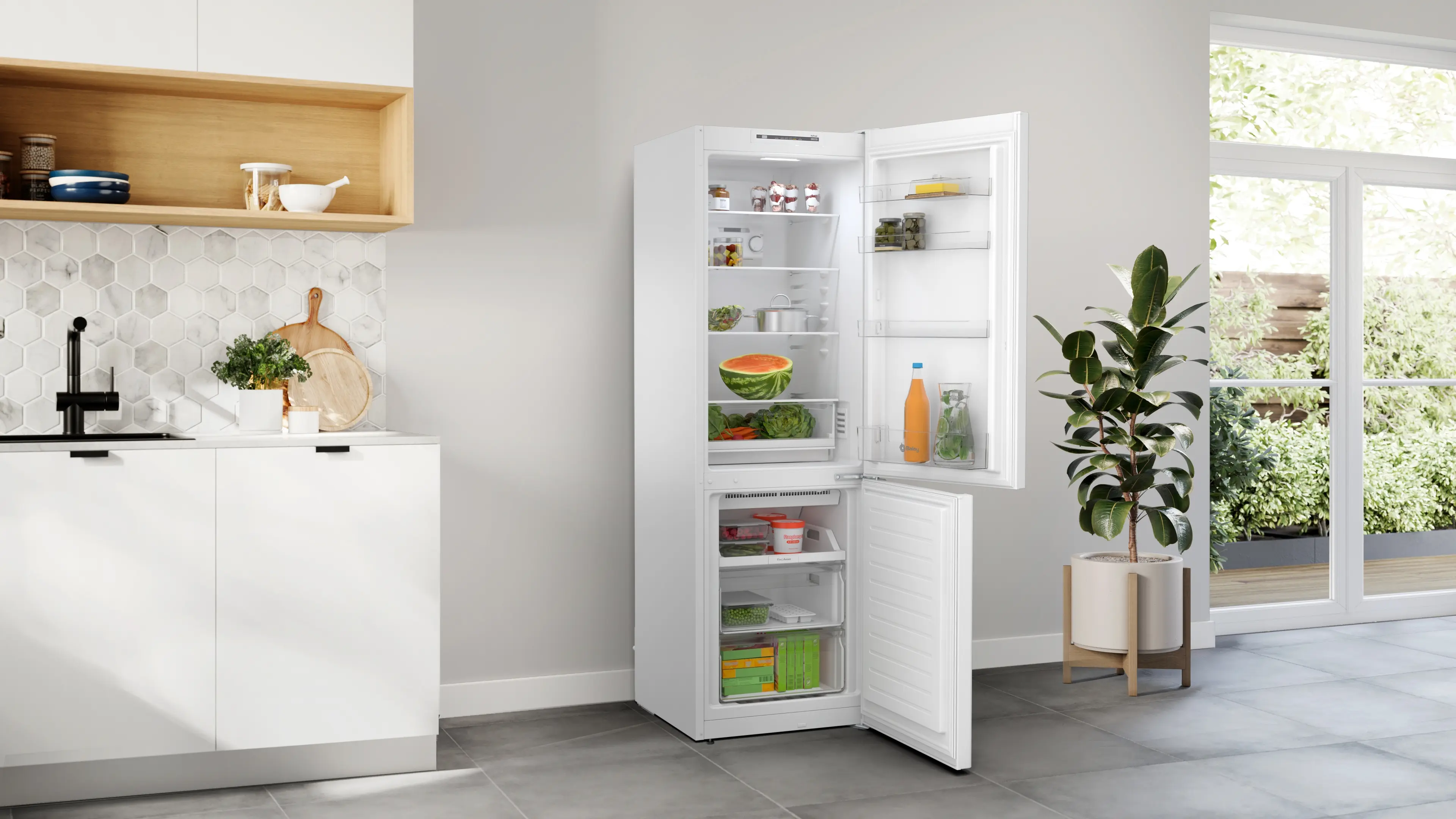 Frigorífico blanco en cocina luminosa con puerta abierta, con comida, junto a una planta en maceta.