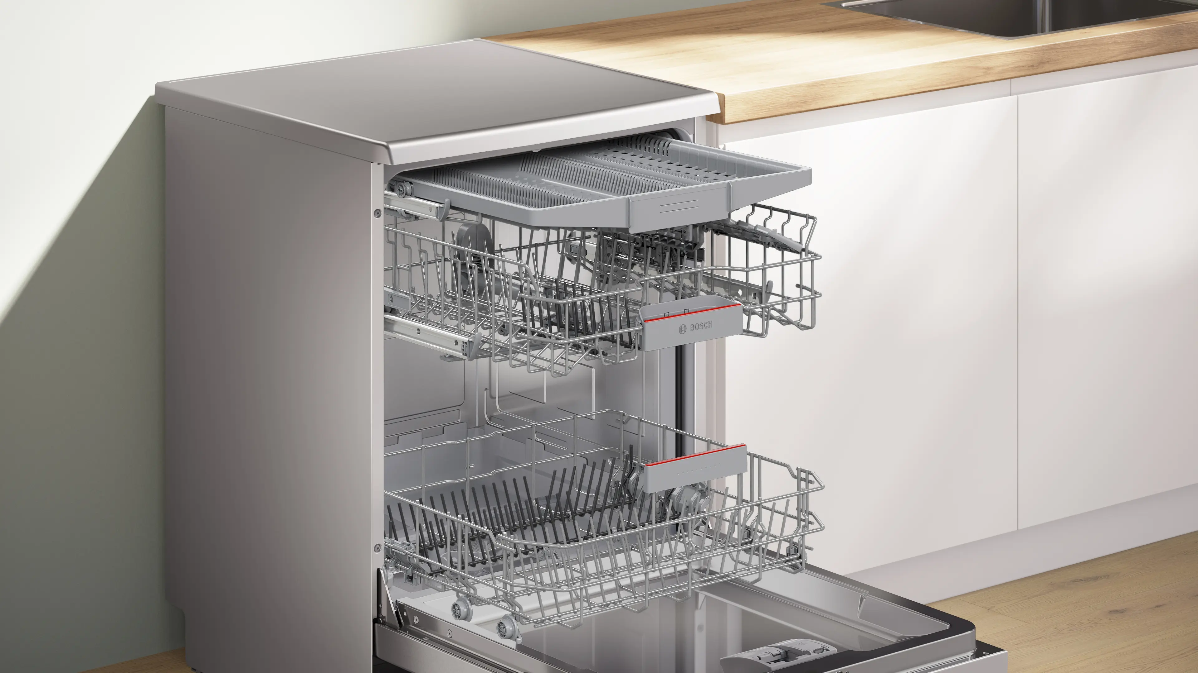 Lavavajillas de acero inoxidable con puerta abierta y tres bandejas extraíbles vacías en cocina.