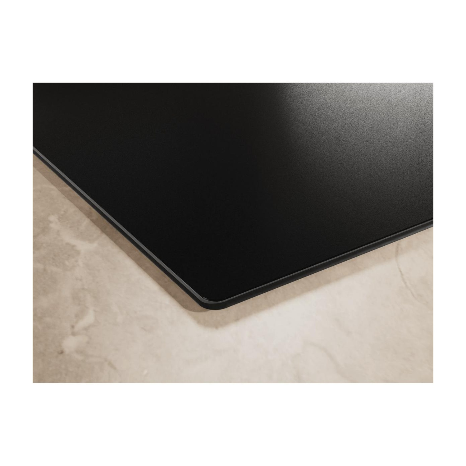 Primo piano dell'angolo di un piano cottura a induzione nero su un piano di lavoro in marmo beige.