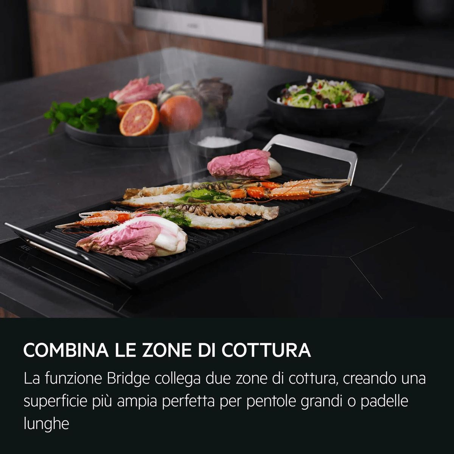 Frutti di mare e carne grigliati su piano cottura a induzione nero con insalata e frutta.