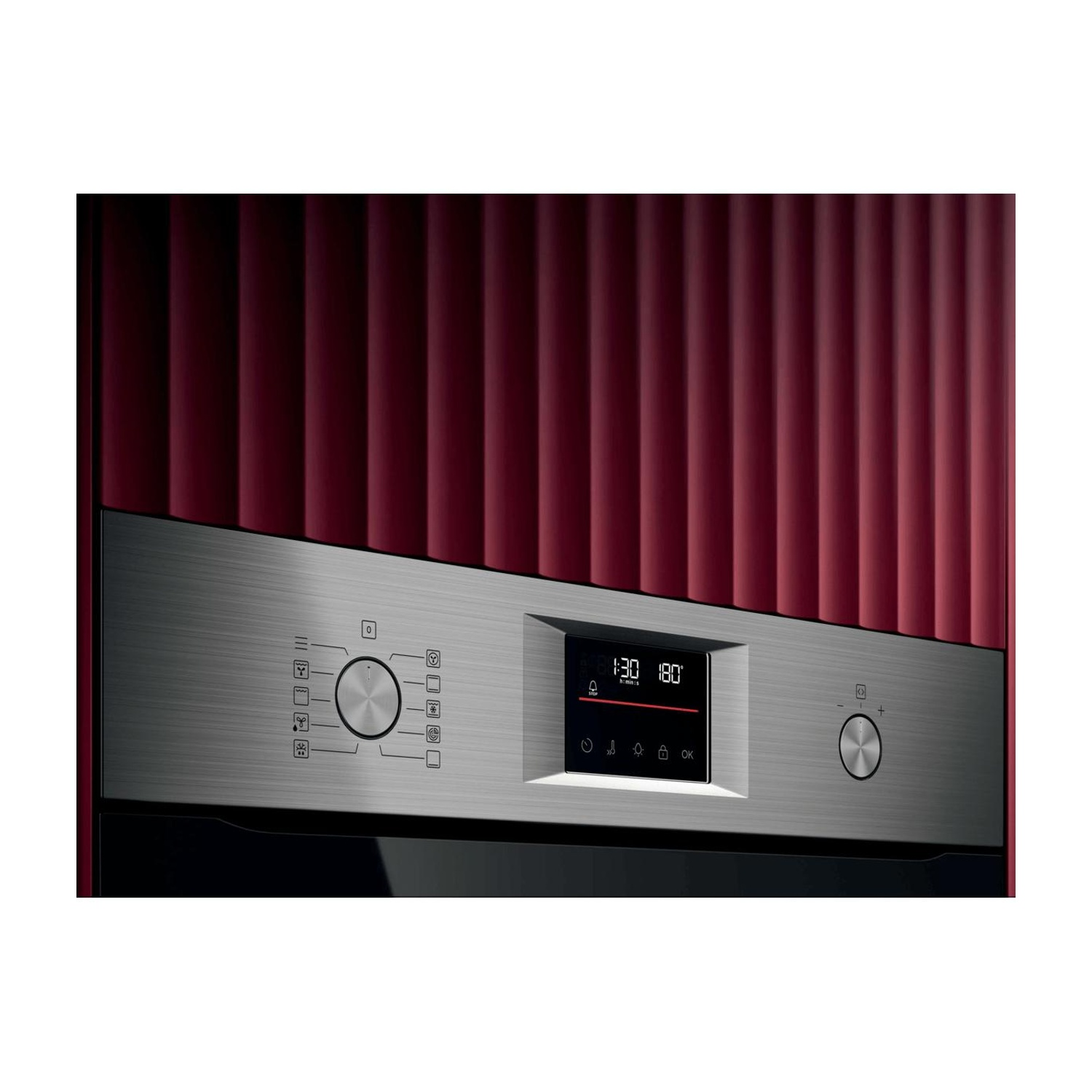 Pannello di controllo forno in acciaio inox con display digitale e manopole su parete rossa.
