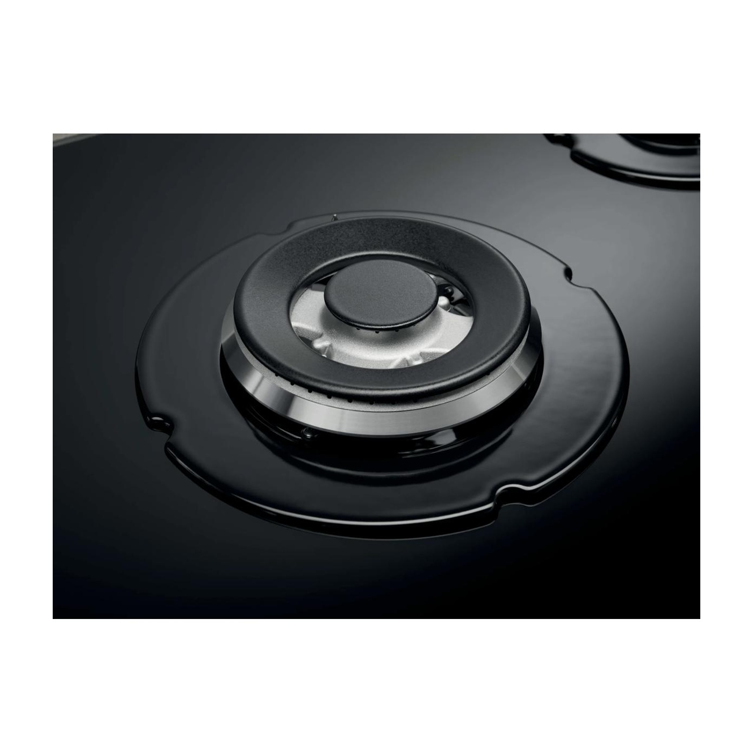 Primo piano di un moderno bruciatore a gas nero con un anello metallico lucido su superficie in vetro.