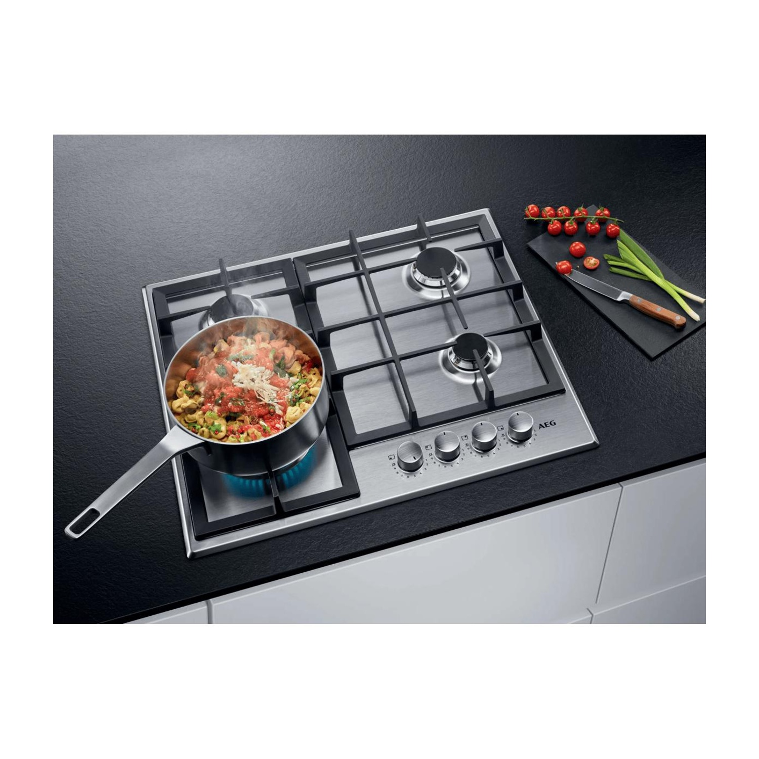 Una pentola di pasta e salsa di pomodoro cuoce su un moderno piano cottura a gas su un piano di lavoro nero.