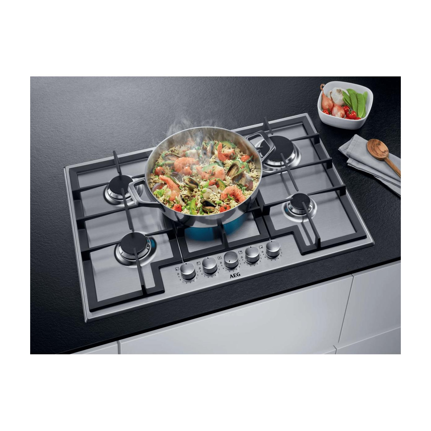 Una pentola di paella fumante si trova su un moderno piano cottura a gas in acciaio inox.