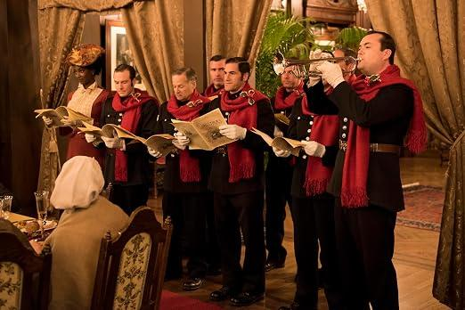 Eine Gruppe von Sternsingern in dunklen Uniformen und roten Schals singt und musiziert drinnen.