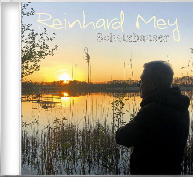 Ein Mann blickt bei Sonnenuntergang über einen ruhigen See mit Schilf im Vordergrund.