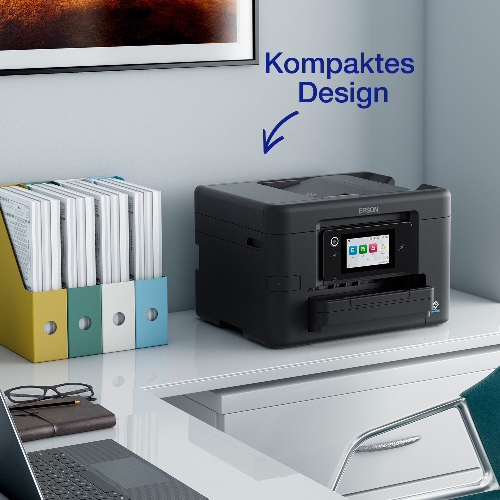 Ein schwarzer Epson-Drucker steht auf einem weißen Schreibtisch neben bunten Aktenordnern und einem Laptop.