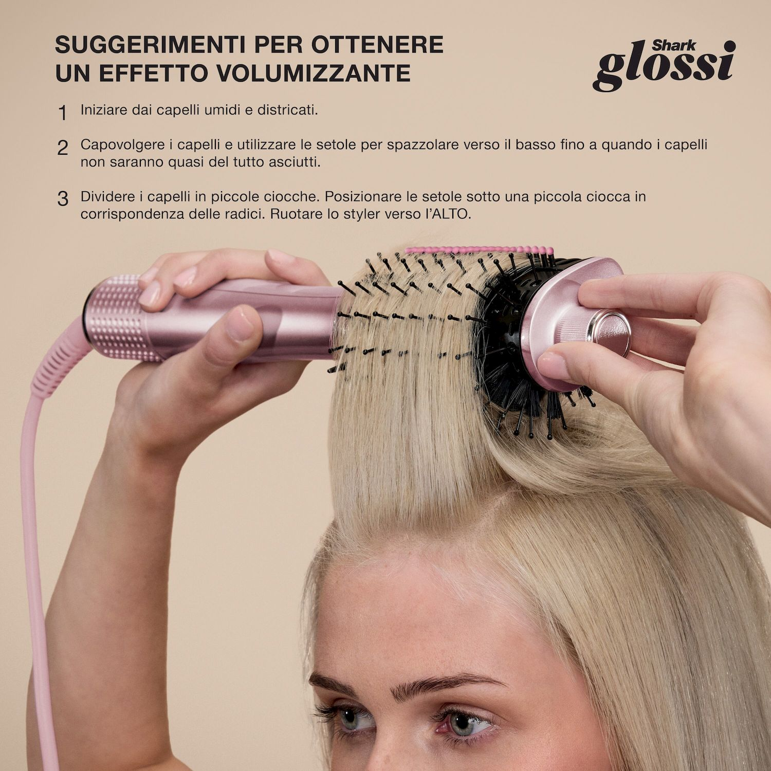Una donna che modella i capelli biondi con una spazzola ad aria calda rosa Shark Glossi, sollevando una ciocca alle radici.