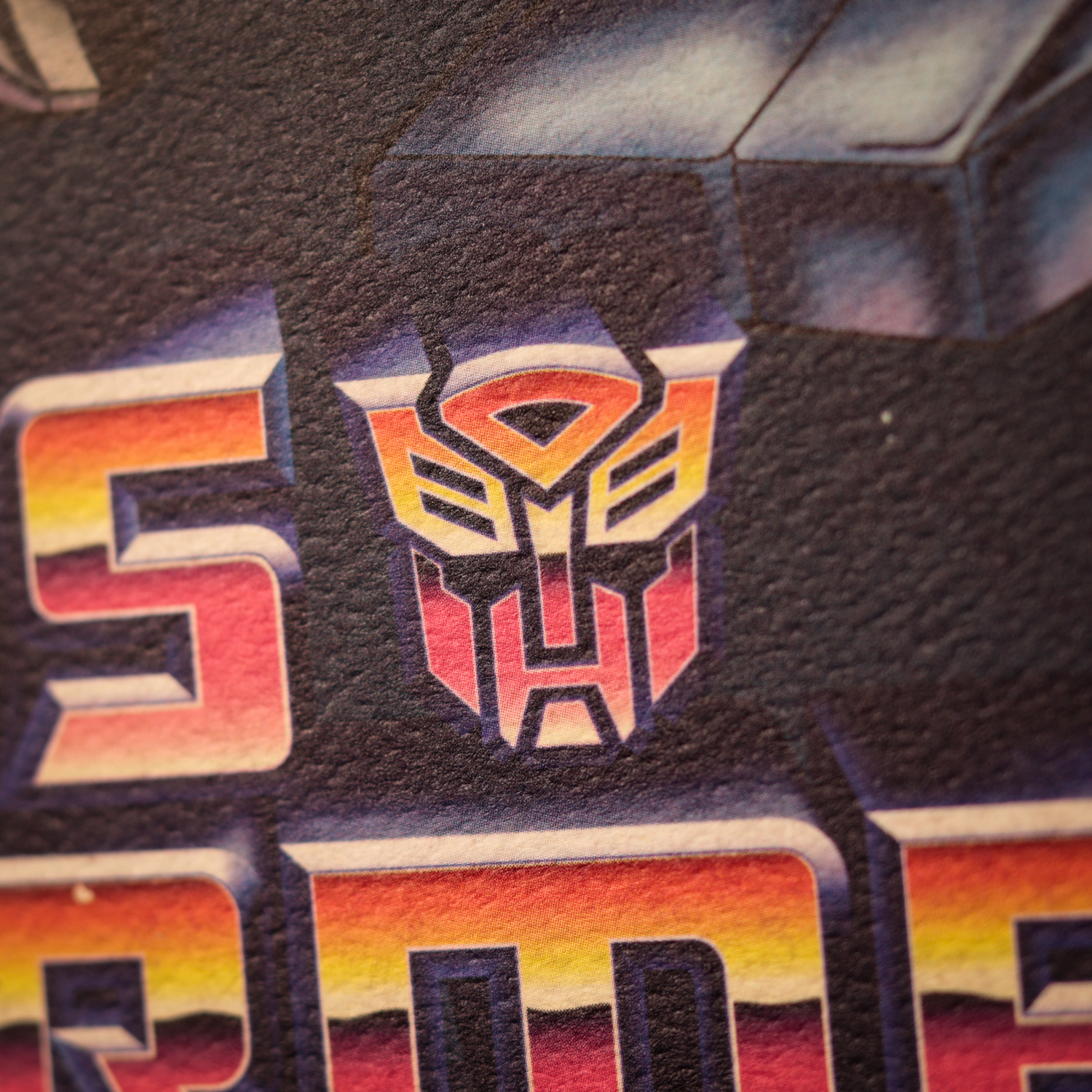 Primer plano del logotipo rojo y amarillo de los Autobots de Transformers sobre fondo oscuro.