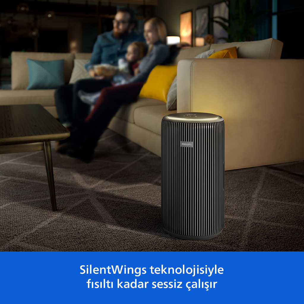 Siyah beyaz Philips hava temizleyici, kanepede oturan bir ailenin bulunduğu oturma odasındaki halıda duruyor.