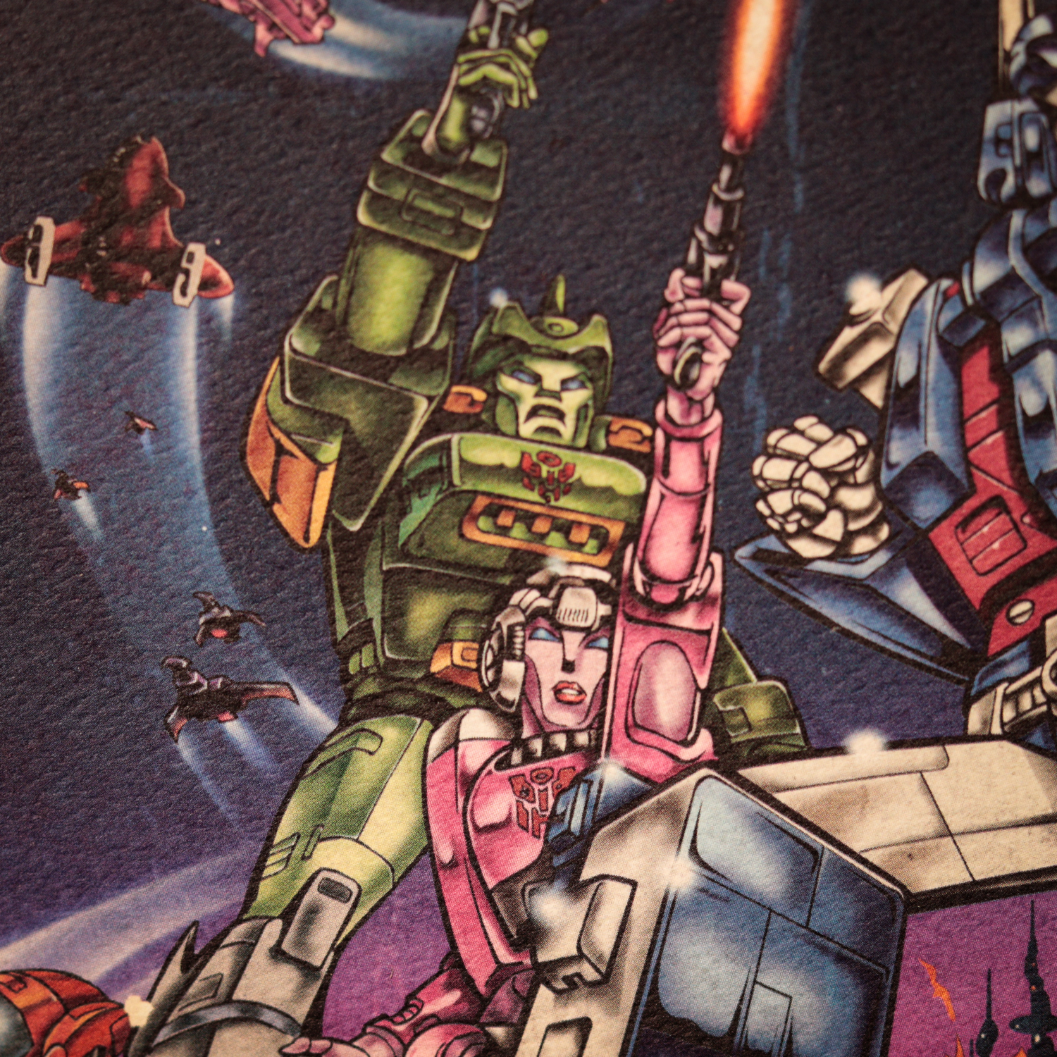 Ilustración retro de Transformers en el espacio con personajes robot verdes, rosas y azules disparando armas.