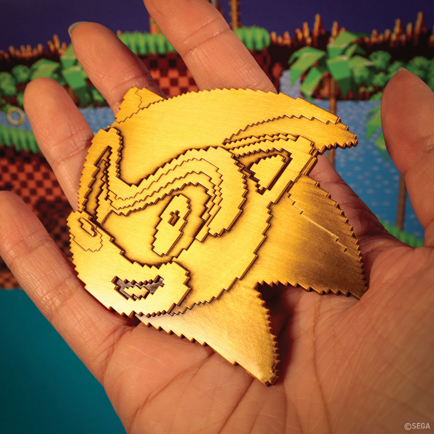 Una mano sosteniendo una talla de madera dorada de Sonic the Hedgehog frente a un fondo de videojuego.
