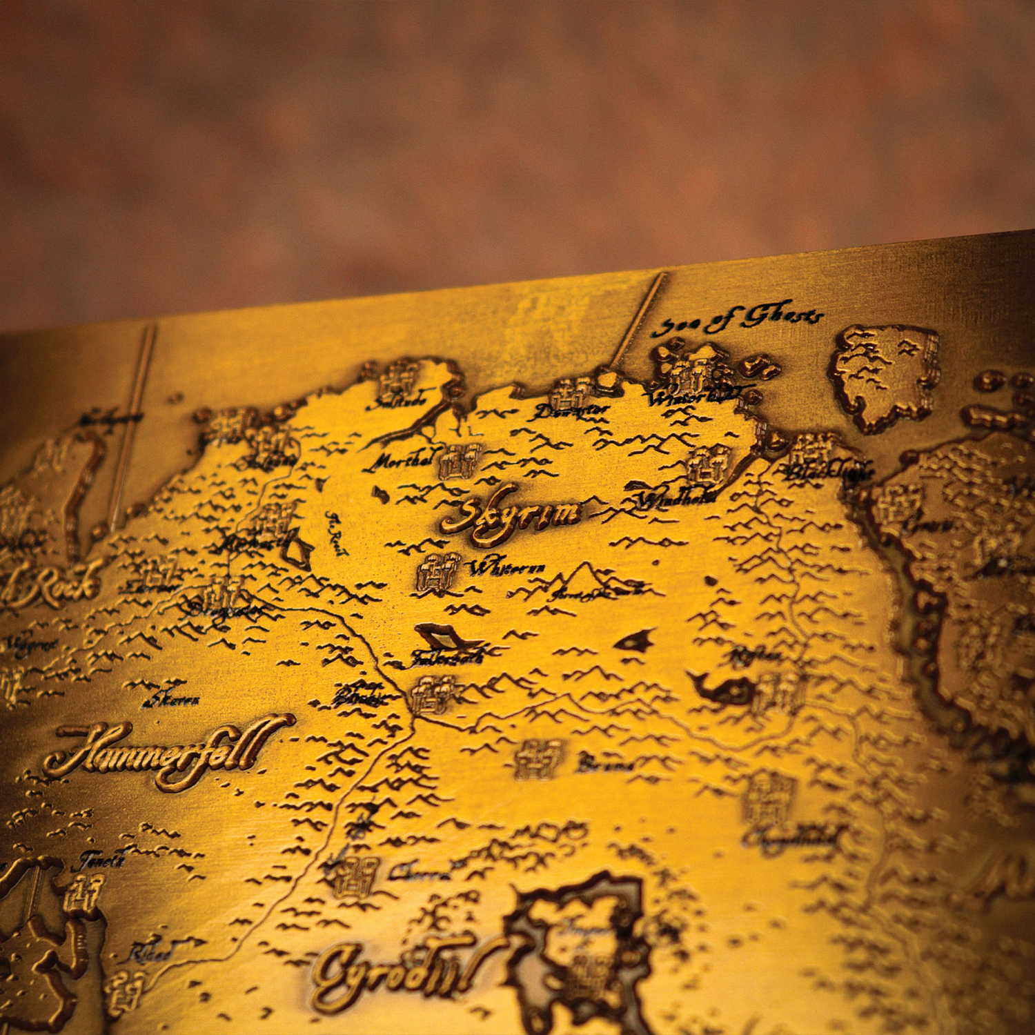 Un mapa detallado de metal dorado muestra las regiones de Skyrim y Cyrodiil de The Elder Scrolls en relieve.