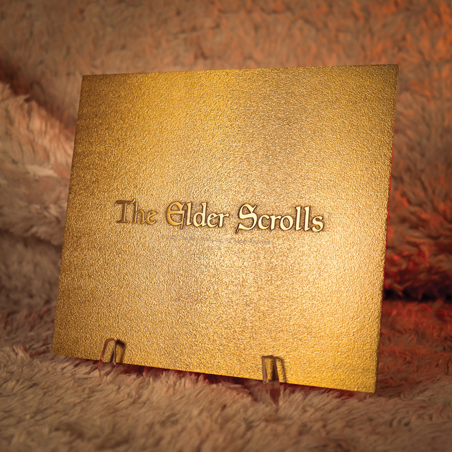 Una placa dorada de The Elder Scrolls sobre un soporte ante un fondo peludo y marrón anaranjado.
