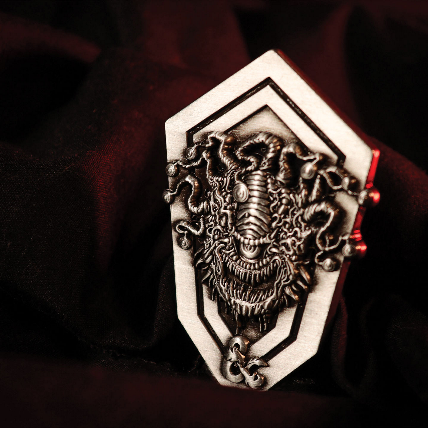 Un pin plateado de Beholder con muchos tentáculos y un gran ojo central sobre tela oscura.