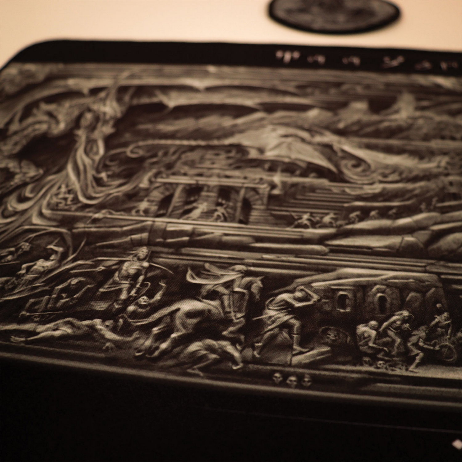 Una imagen en relieve detallada en blanco y negro muestra escenas de fantasía con batallas y criaturas.