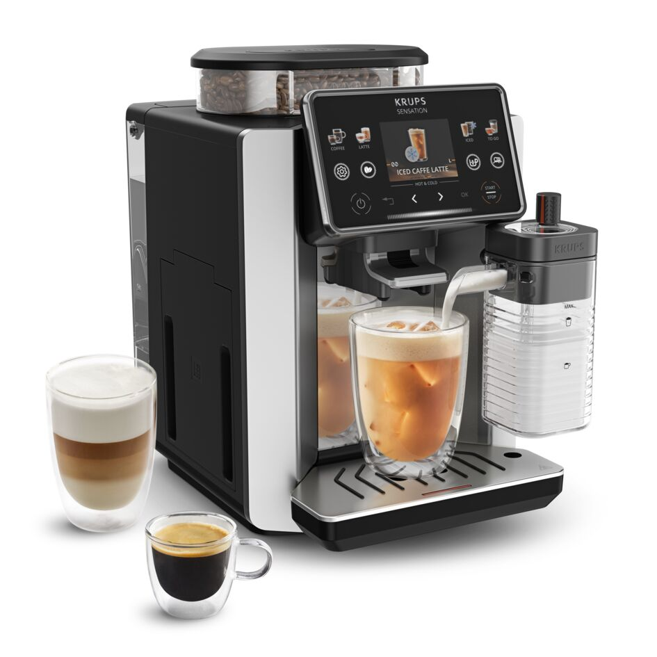 Krups kahve makinesi buzlu kahve bardağına süt dolduruyor. Yakında latte macchiato ve espresso bardakları var.