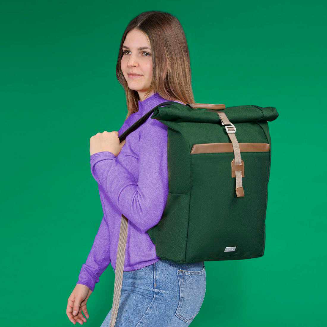 Eine Frau mit lila Pullover trägt einen großen grünen Rucksack vor einem einfarbigen grünen Hintergrund.
