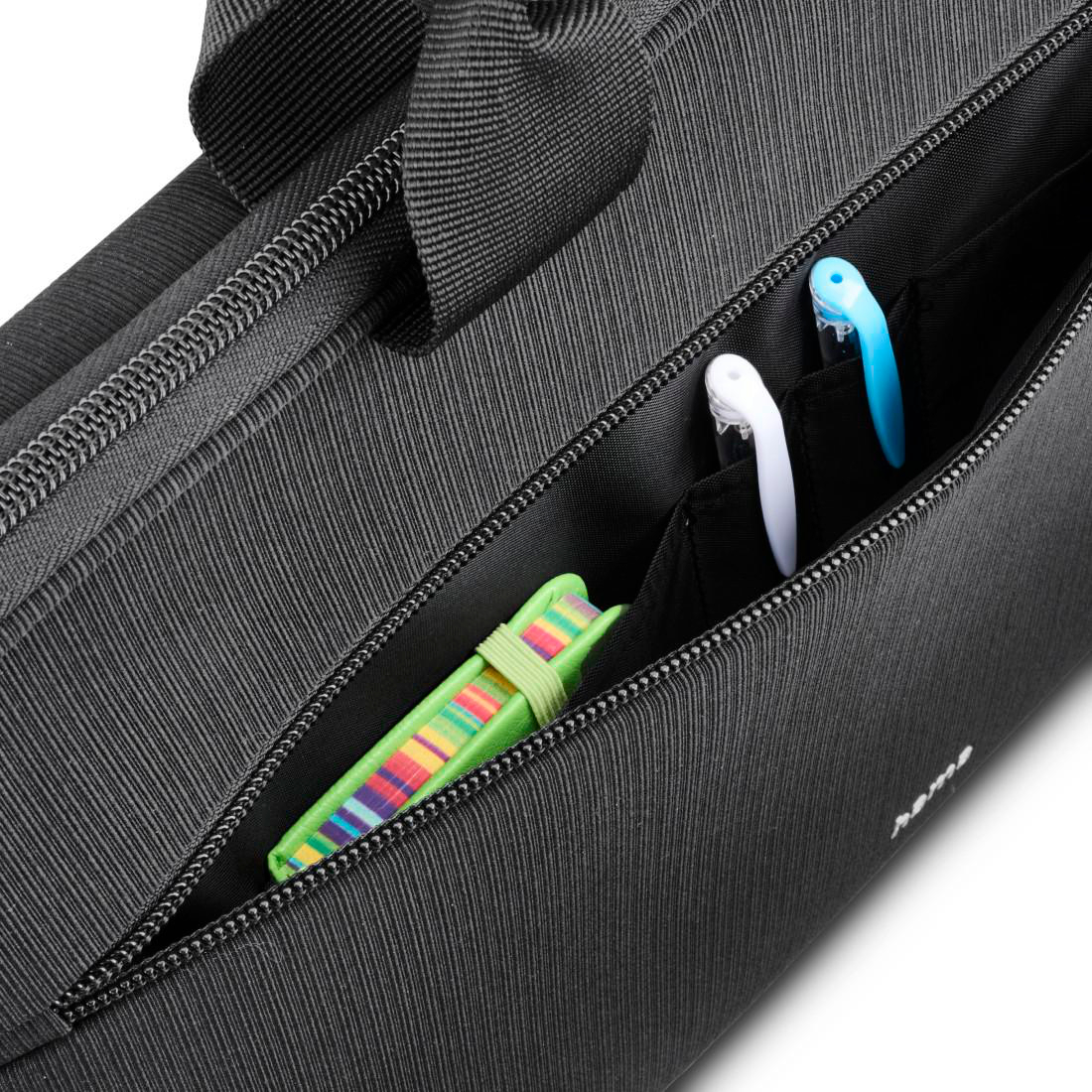 Schwarze Laptoptasche mit geöffneter Vordertasche, in der ein grünes Notizbuch und zwei Stifte stecken.