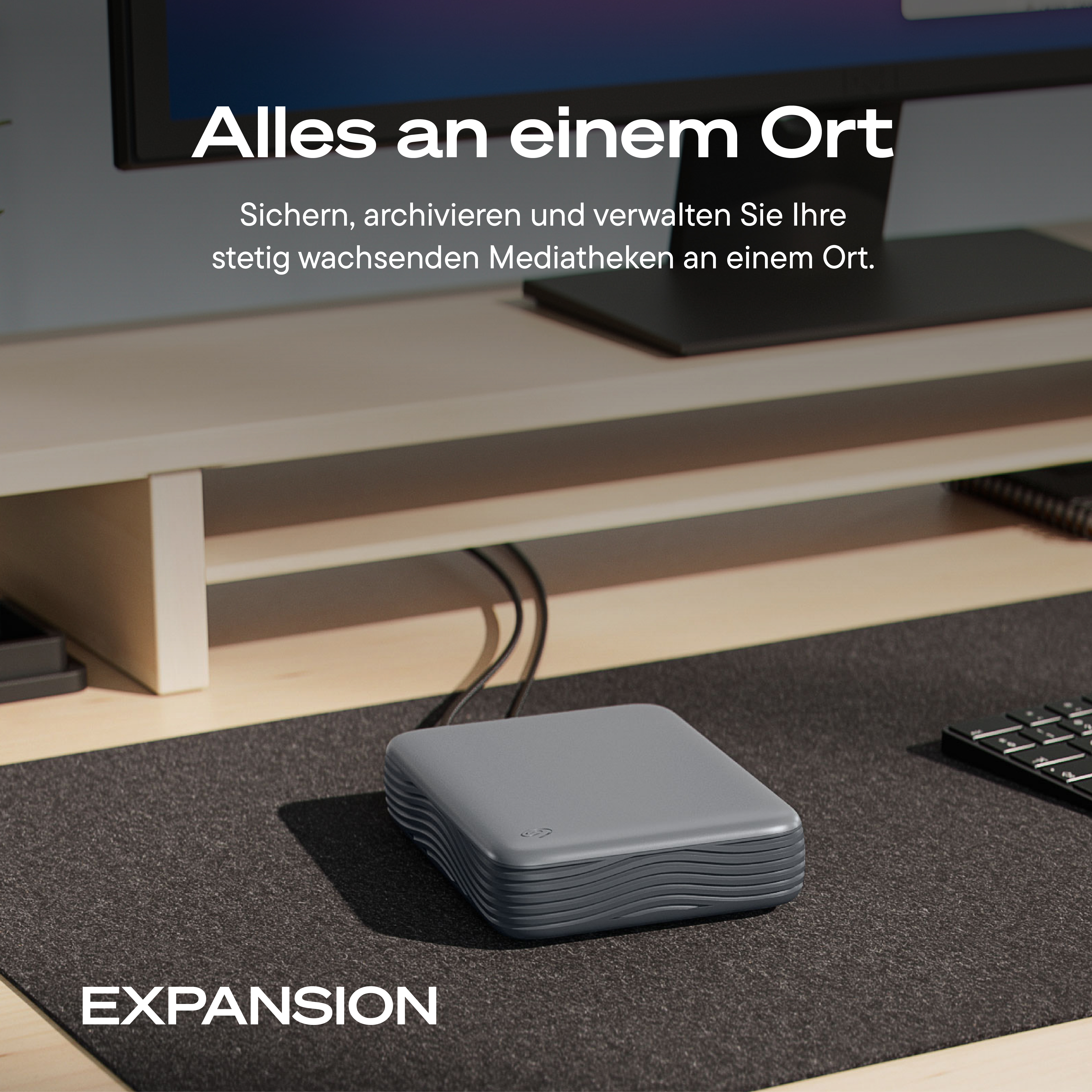 Eine graue externe Festplatte auf einem Schreibtisch unter einem Monitor mit deutschem Text.