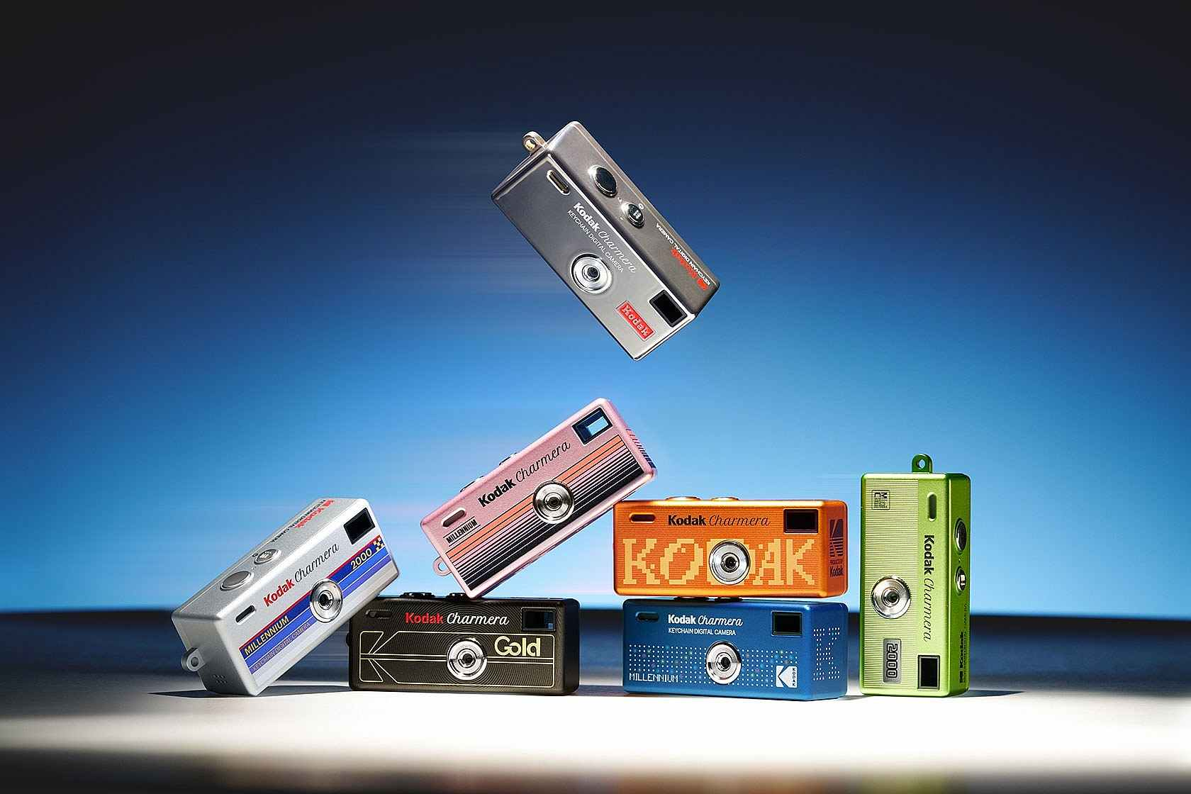 Sept mini caméras numériques Kodak Charmera colorées disposées sur fond blanc avec dégradé bleu.