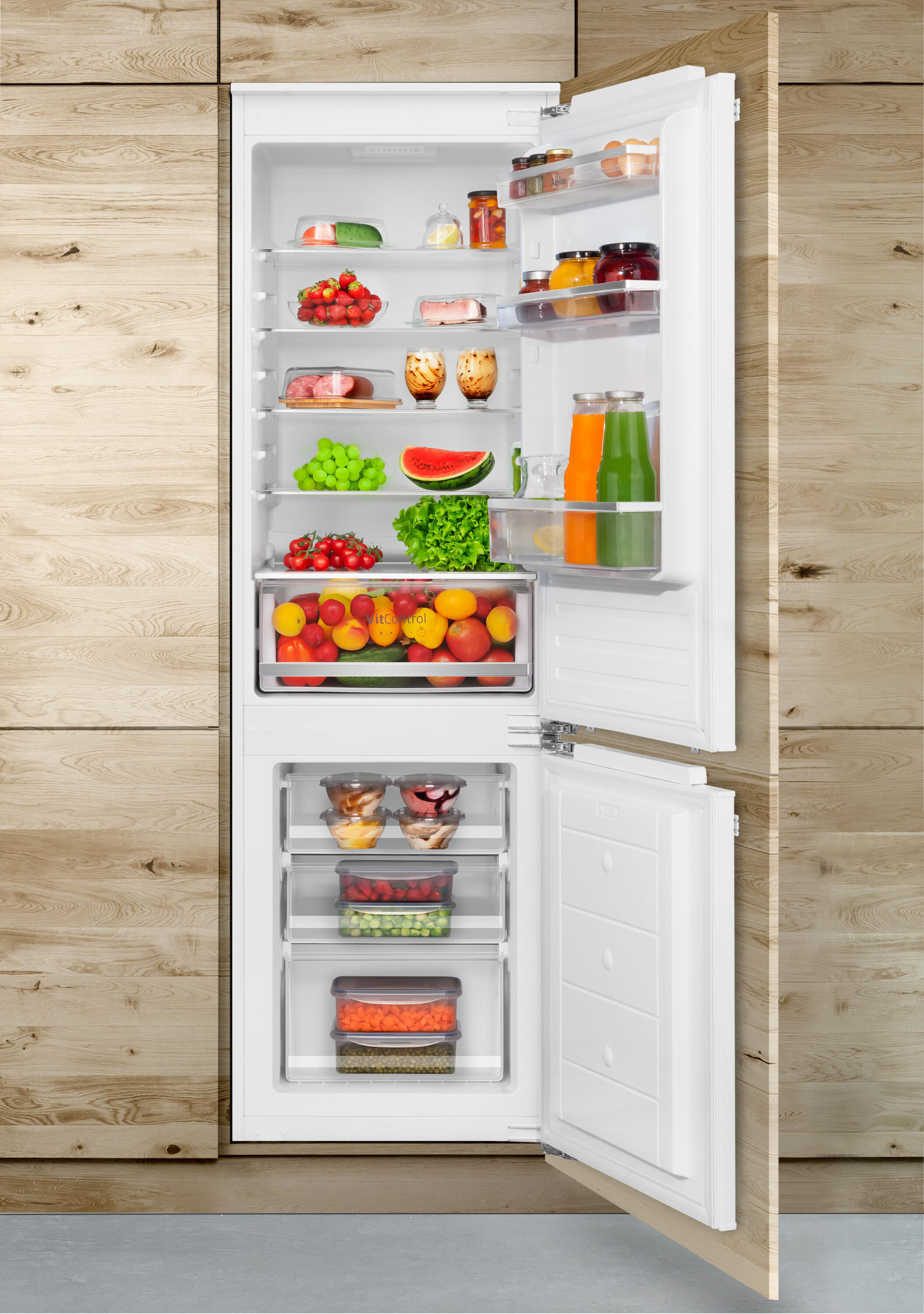 Ein weißer, offener Einbaukühlschrank in Holzoptik ist reichlich mit frischem Obst, Gemüse und Säften gefüllt.