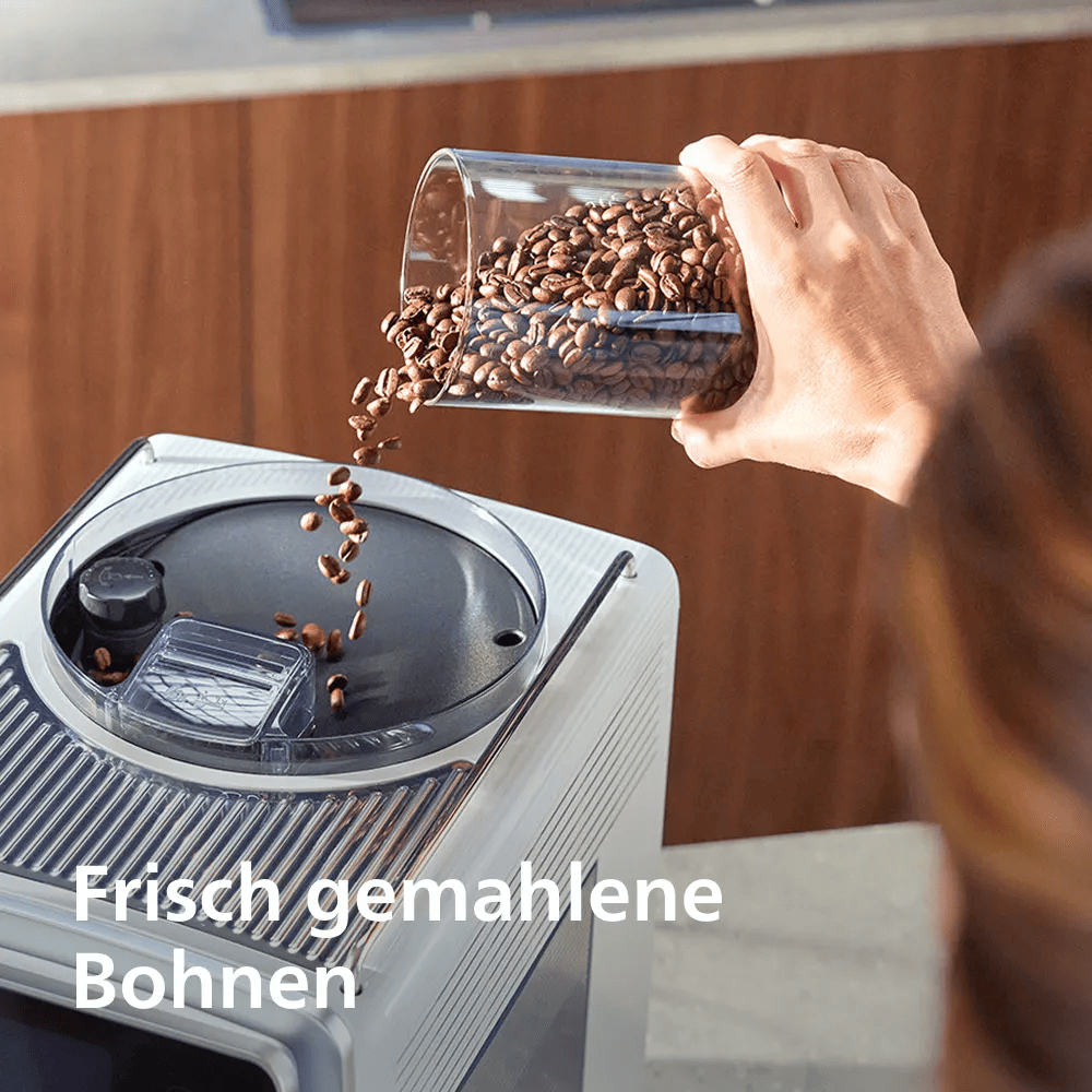 Eine Hand schüttet Kaffeebohnen aus einem Glas in den Behälter einer Kaffeemaschine.