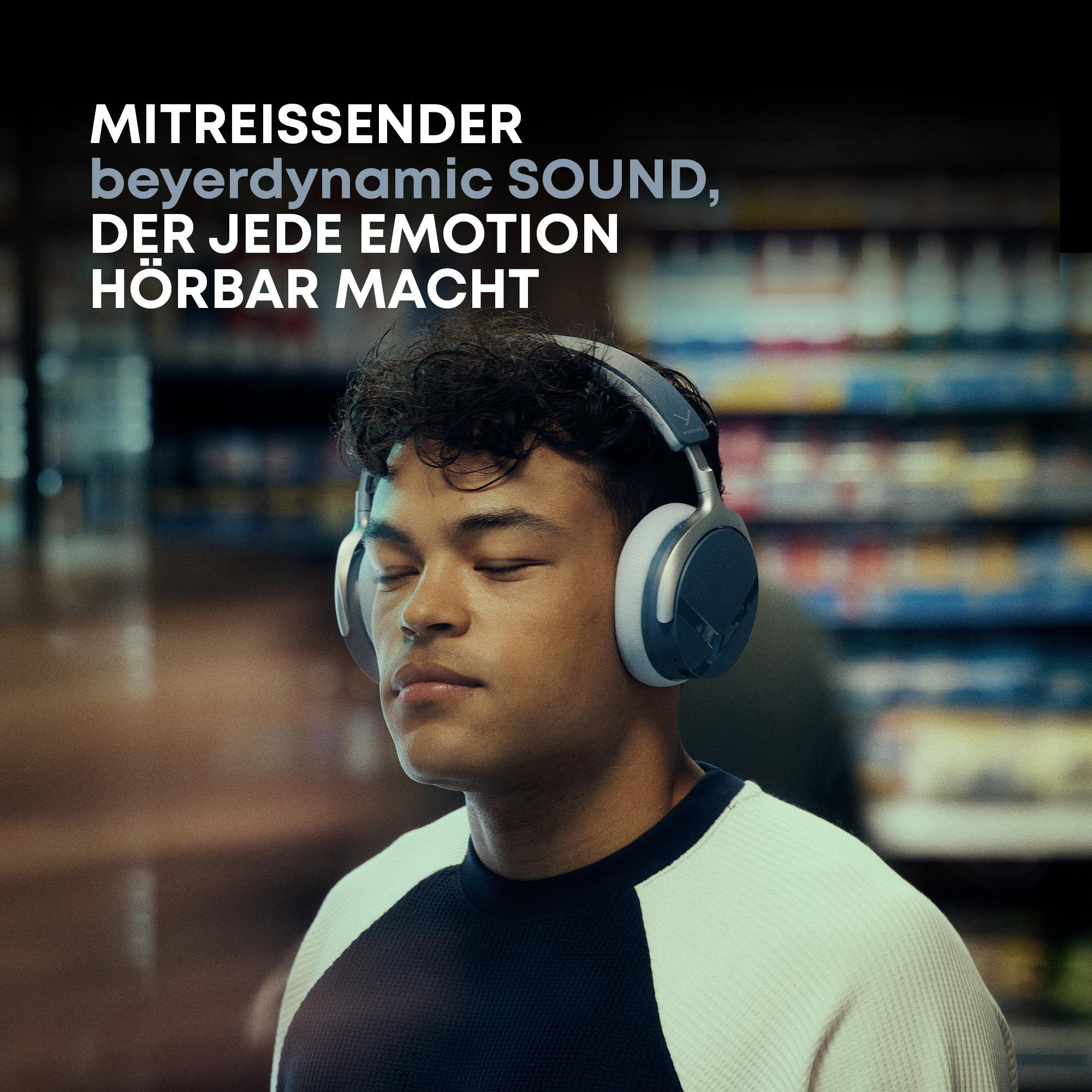Ein junger Mann mit geschlossenen Augen trägt graue Beyerdynamic-Kopfhörer in einem Geschäft.