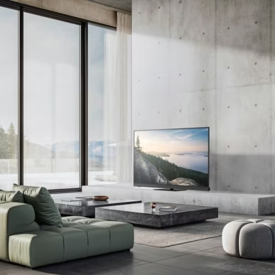 Modern nappali TV-vel, zöld kanapéval, szürke puffal, alacsony asztalokkal és nagy ablakokkal egy betonfal előtt.