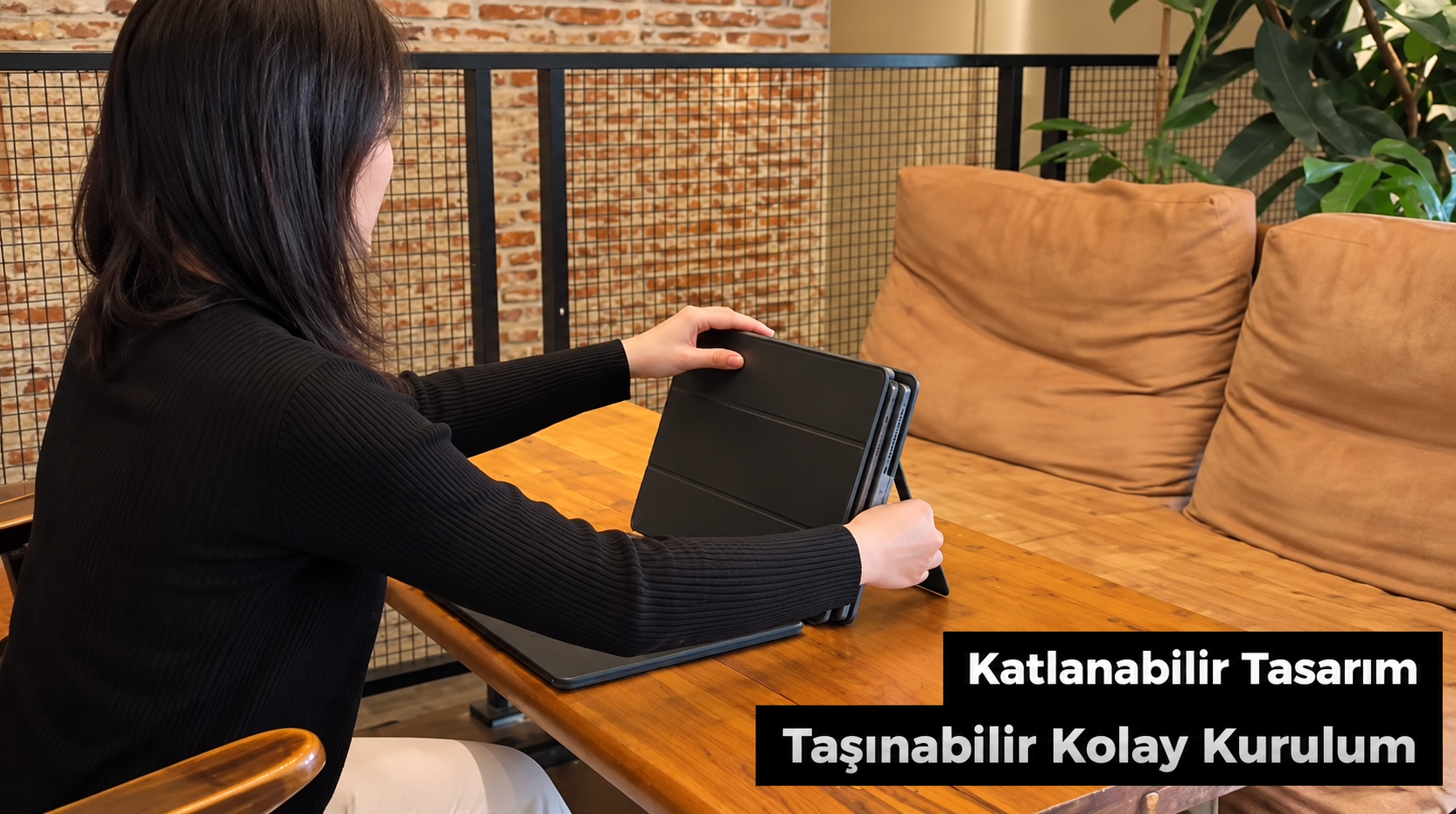 Ahşap masada oturan bir kadın, kılıflı siyah tableti açıyor.