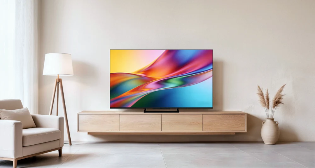 Egy nagy tévé egy fa szekrényen egy világos, minimalista nappaliban lámpával és vázával.