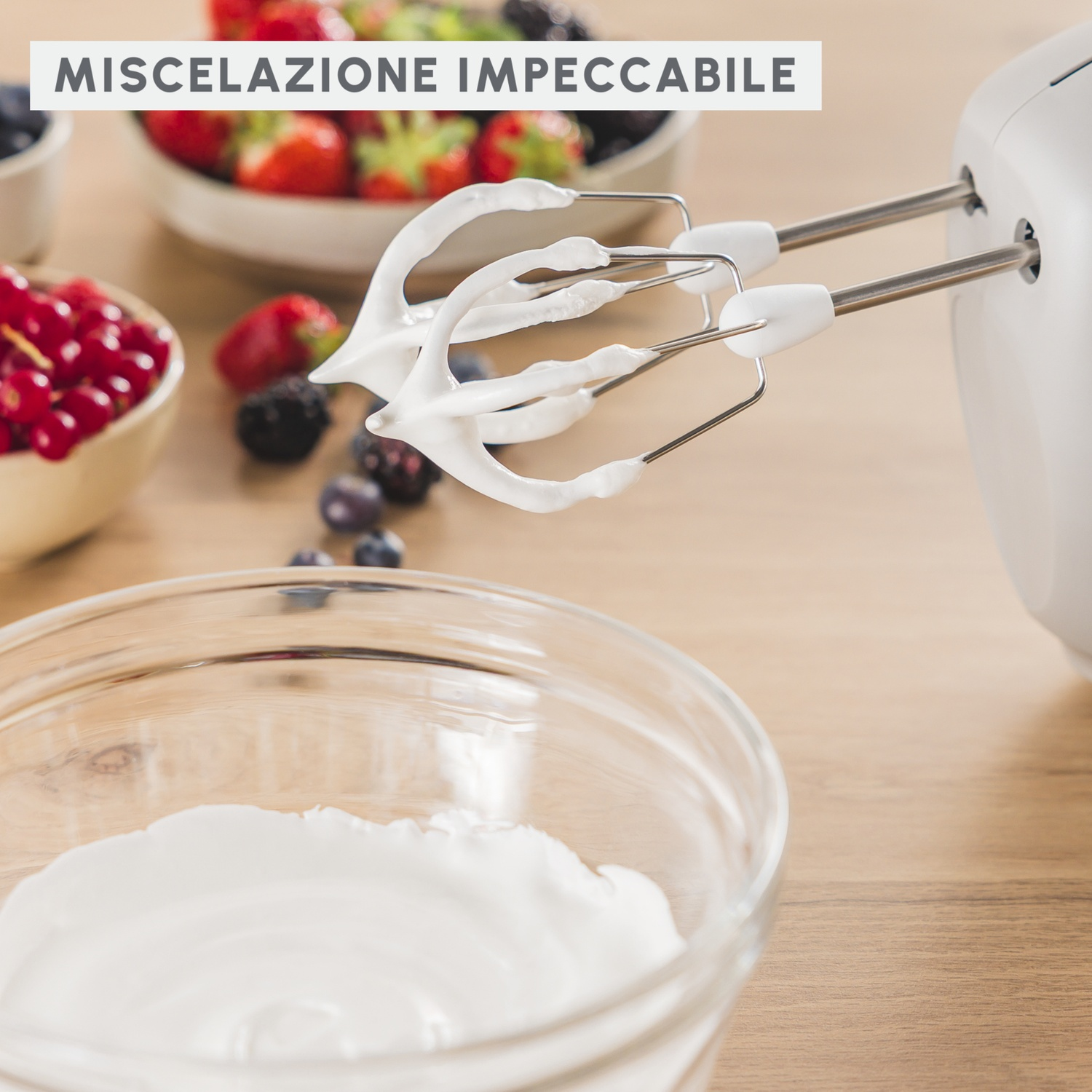 Sbattitore elettrico con panna montata sulle fruste sopra una ciotola, con bacche e tavolo in legno.