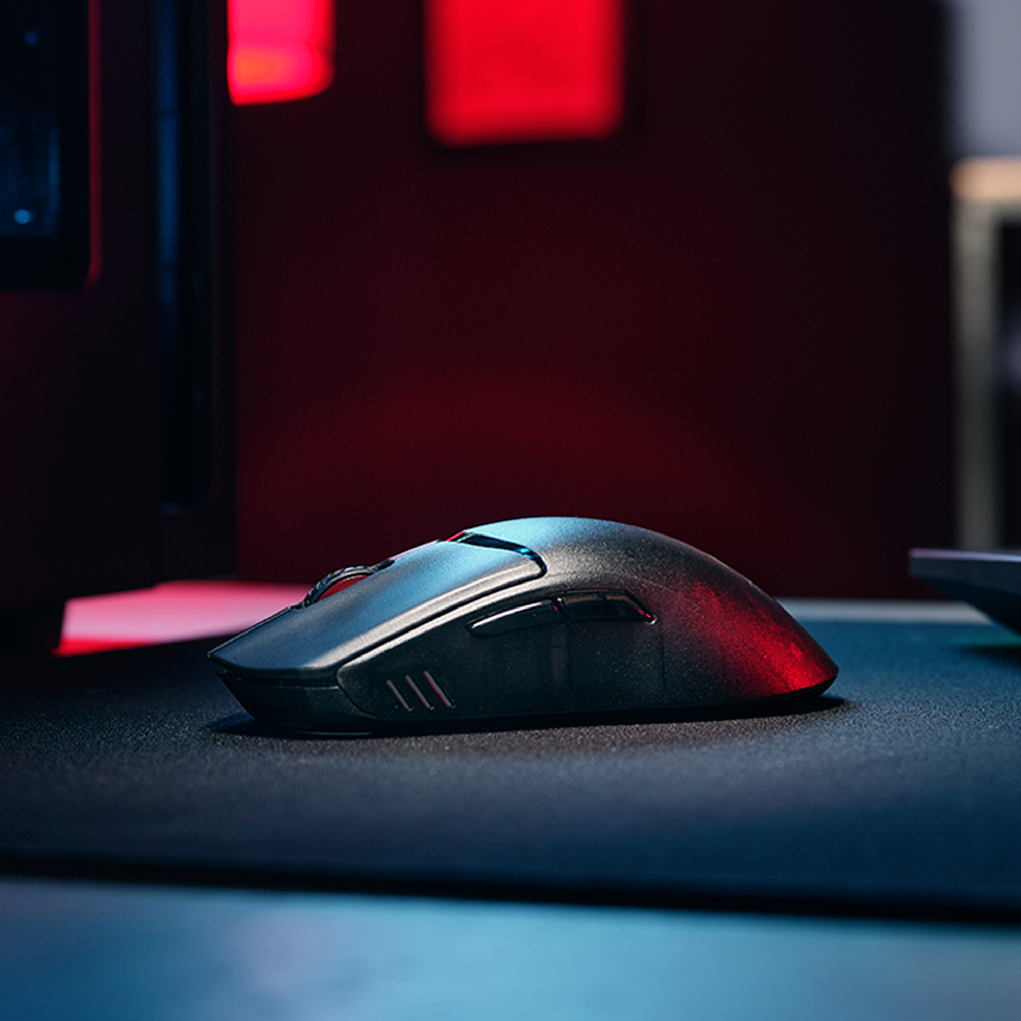 Eine schwarze Gaming-Maus steht auf einem Mauspad vor rotem und blauem Hintergrund.